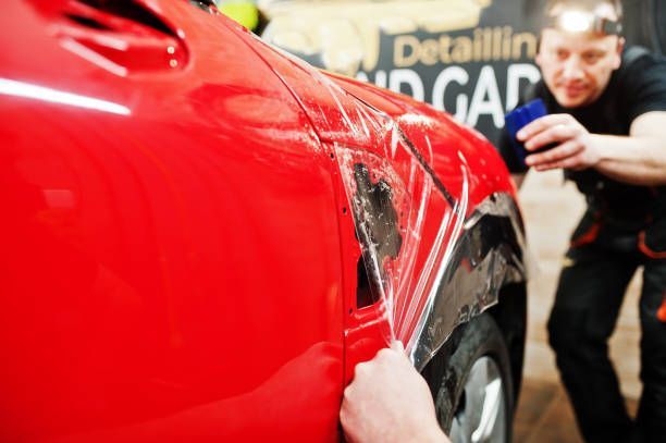 Person applying protective film to a red car fender in a detail shop.