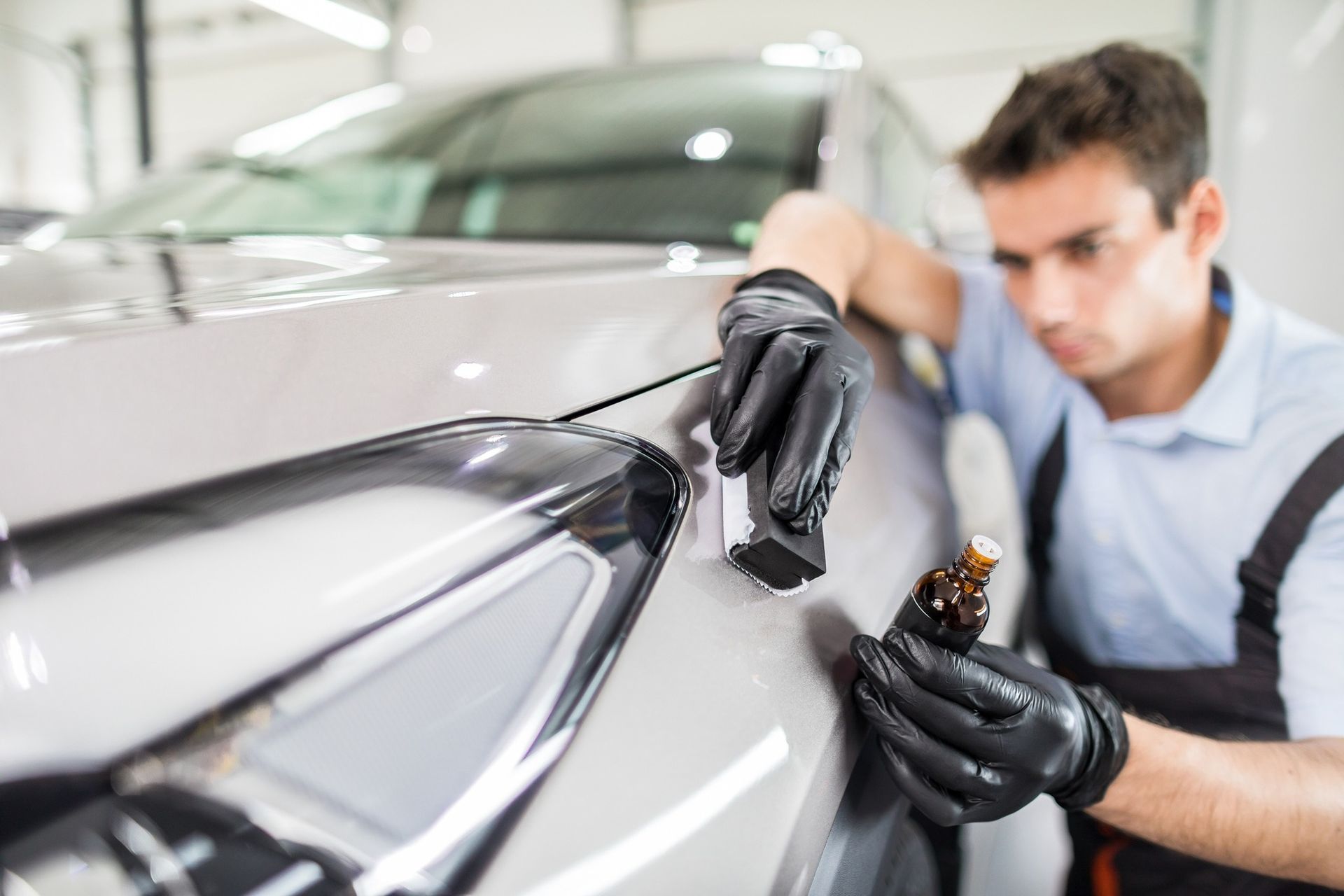 Man applying ceramic coating to a car's hood, wearing black gloves.