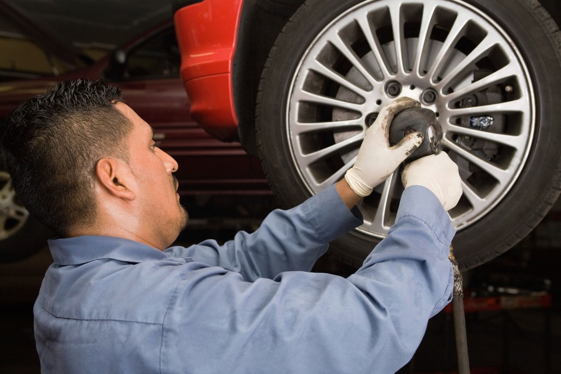Mechanic using an impact wrench to remove a car tire in a garage.