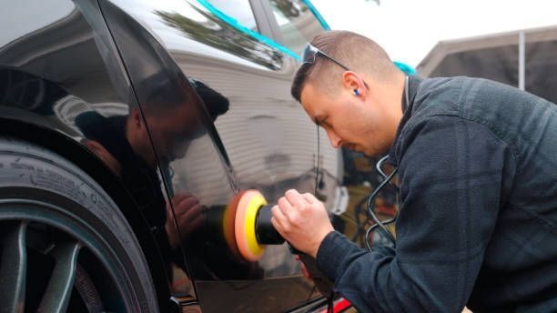 Man polishes a black car with a power buffer outdoors.