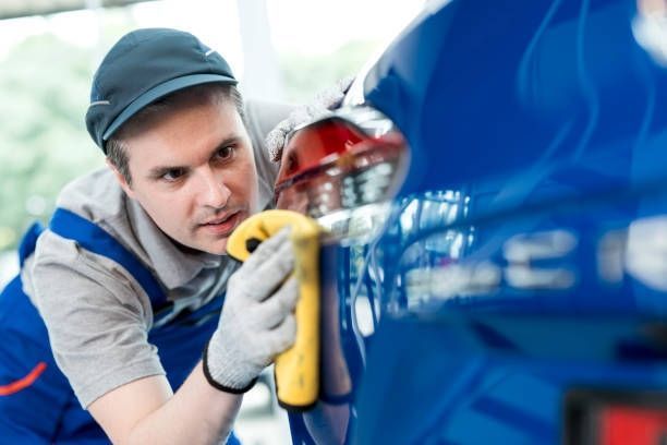 Person polishing blue car with a yellow cloth.