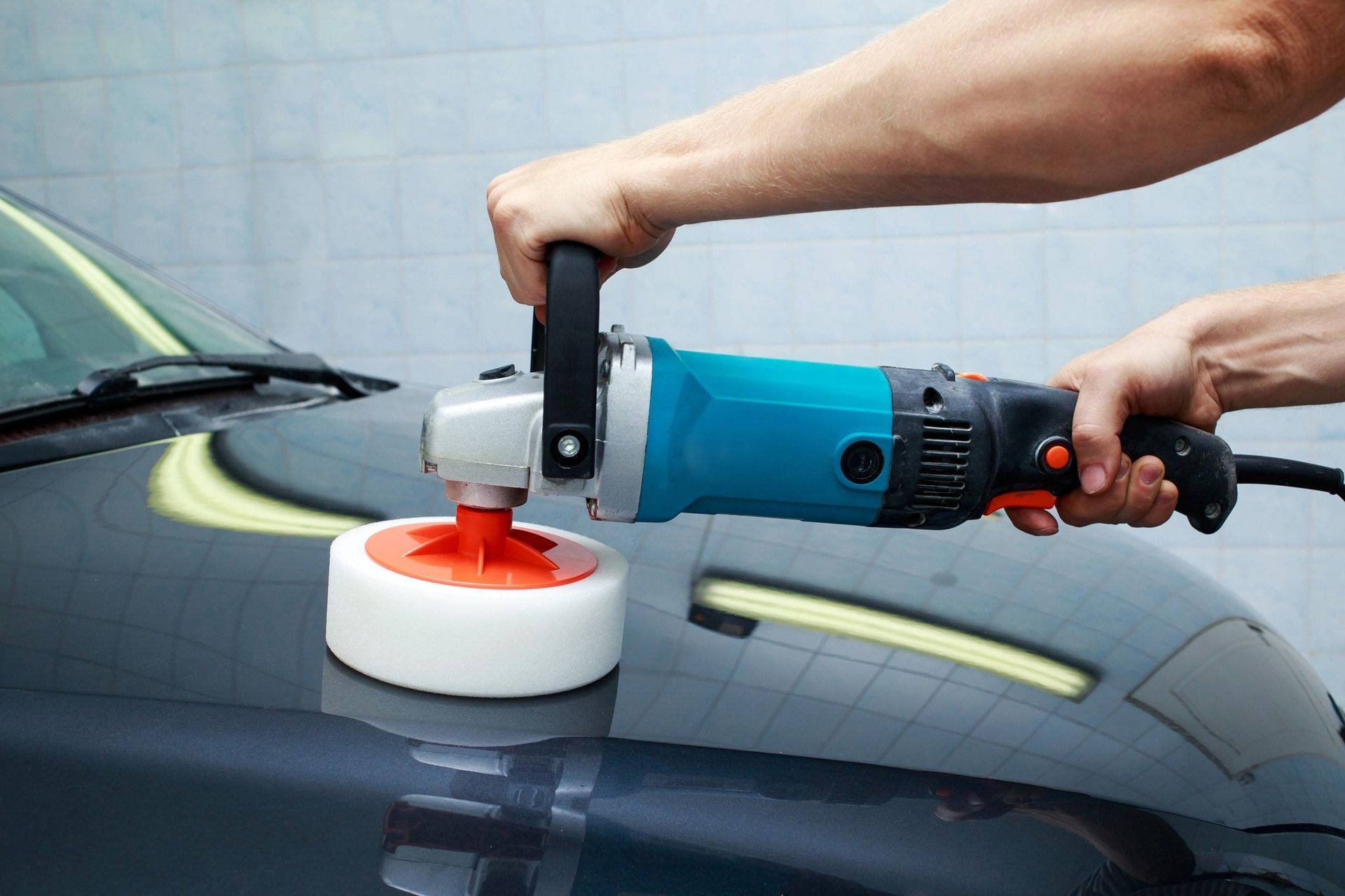 Person using an electric polisher on a dark car; white and red buffing pad.