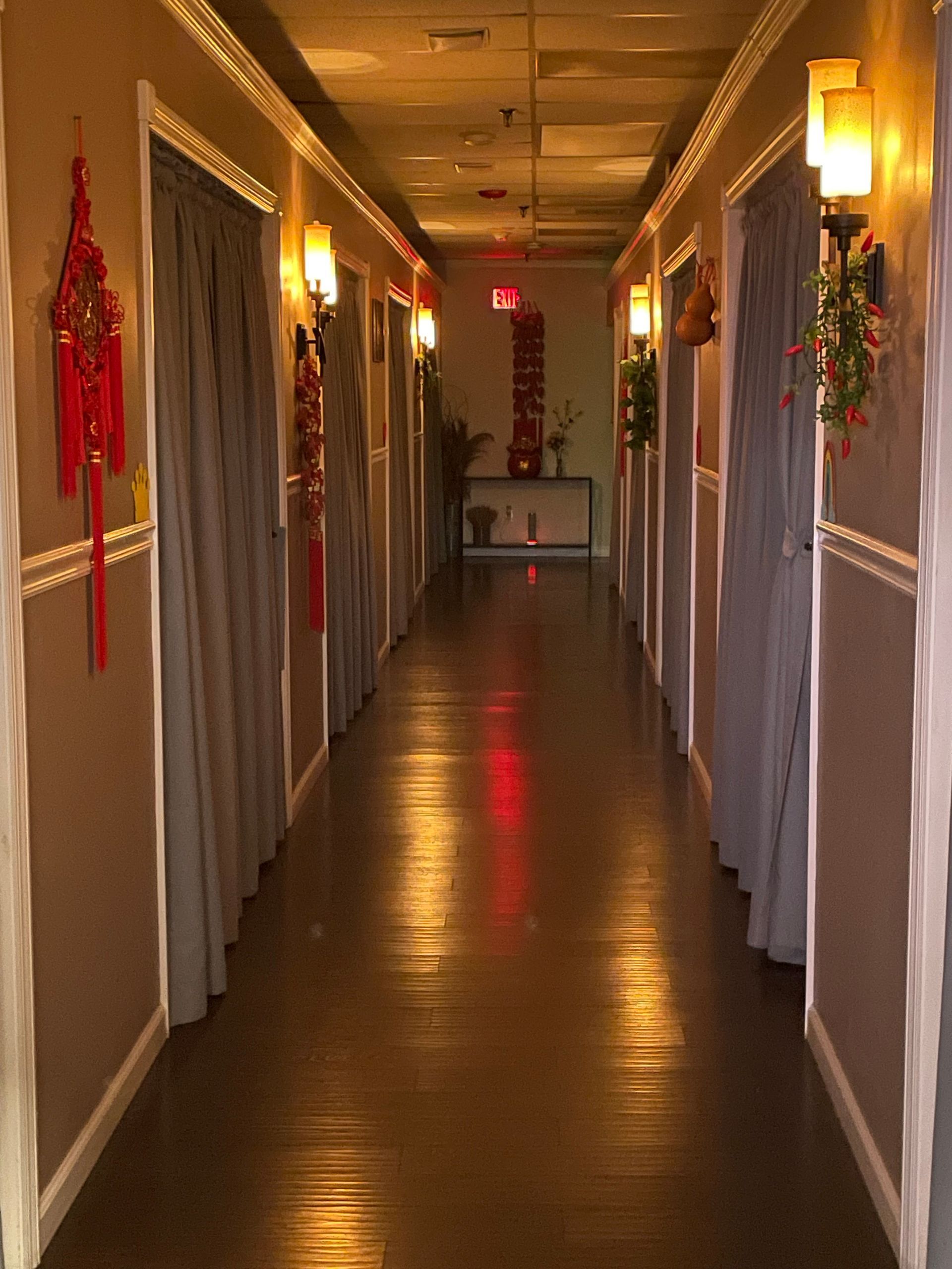 Long hallway with doors, sconce lighting, and decorative red hangings.
