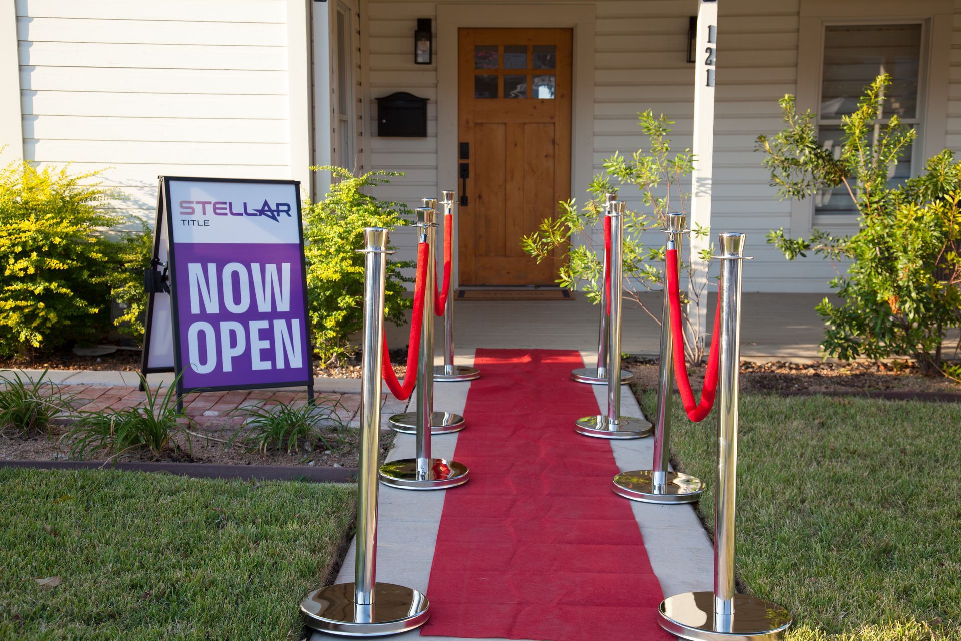 A red carpet leads to a house with a sign that says now open.