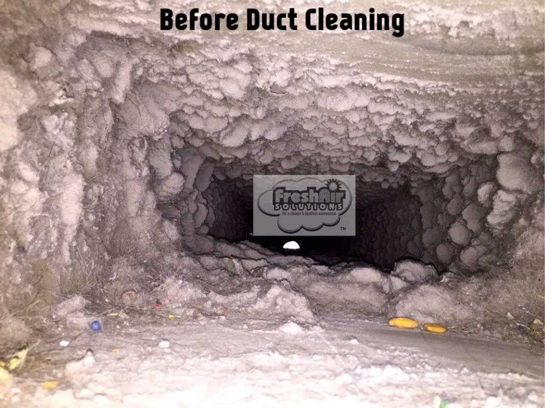 Duct interior before cleaning; filled with debris. Dark, narrow, with a sign in the center.