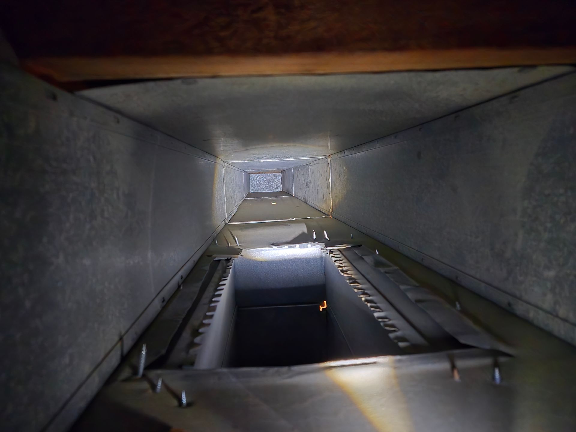 Metal HVAC ductwork, looking down its interior. Duct is gray and rectangular, illuminated by a light source.