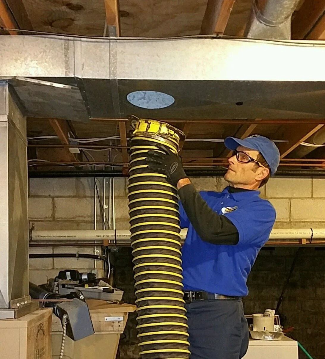 A person in blue shirt installs ductwork in a basement.