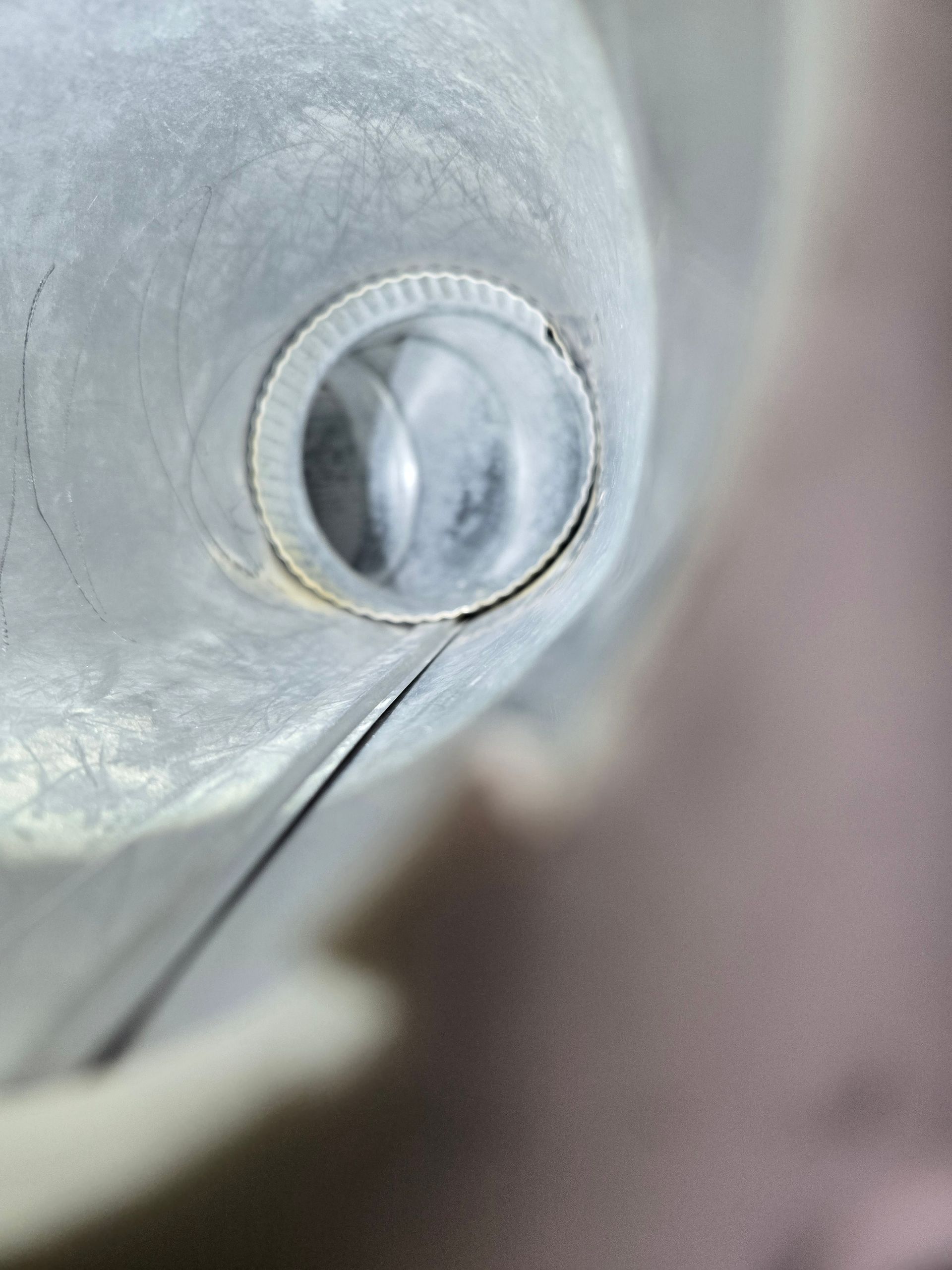 Close-up of a glass or metal tube with a circular opening at the end, set against a pinkish background.