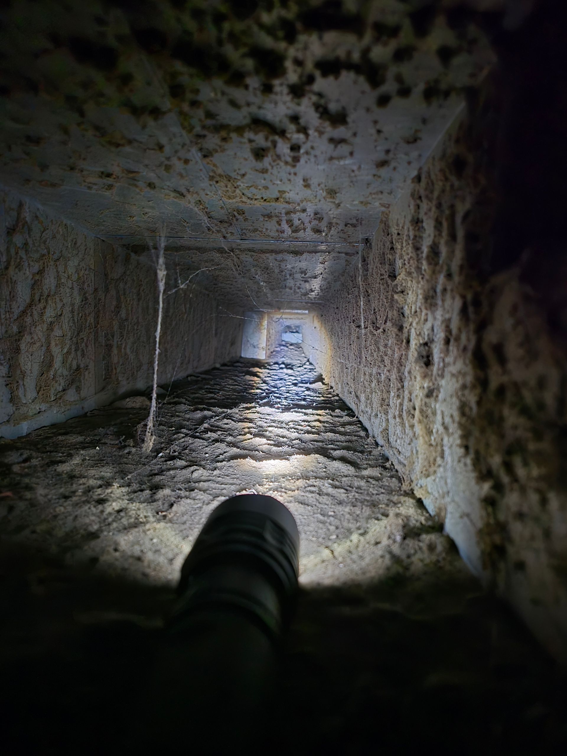 A flashlight illuminates a dirty air duct covered in debris and grime.