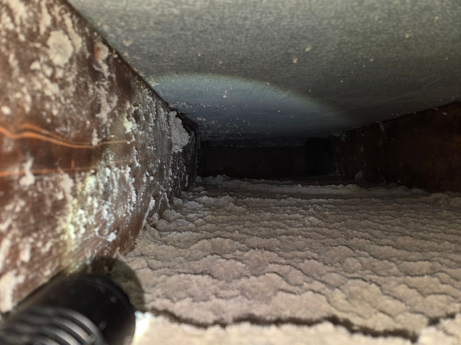 Interior of an air duct heavily coated in white, textured material, illuminated by a flashlight.