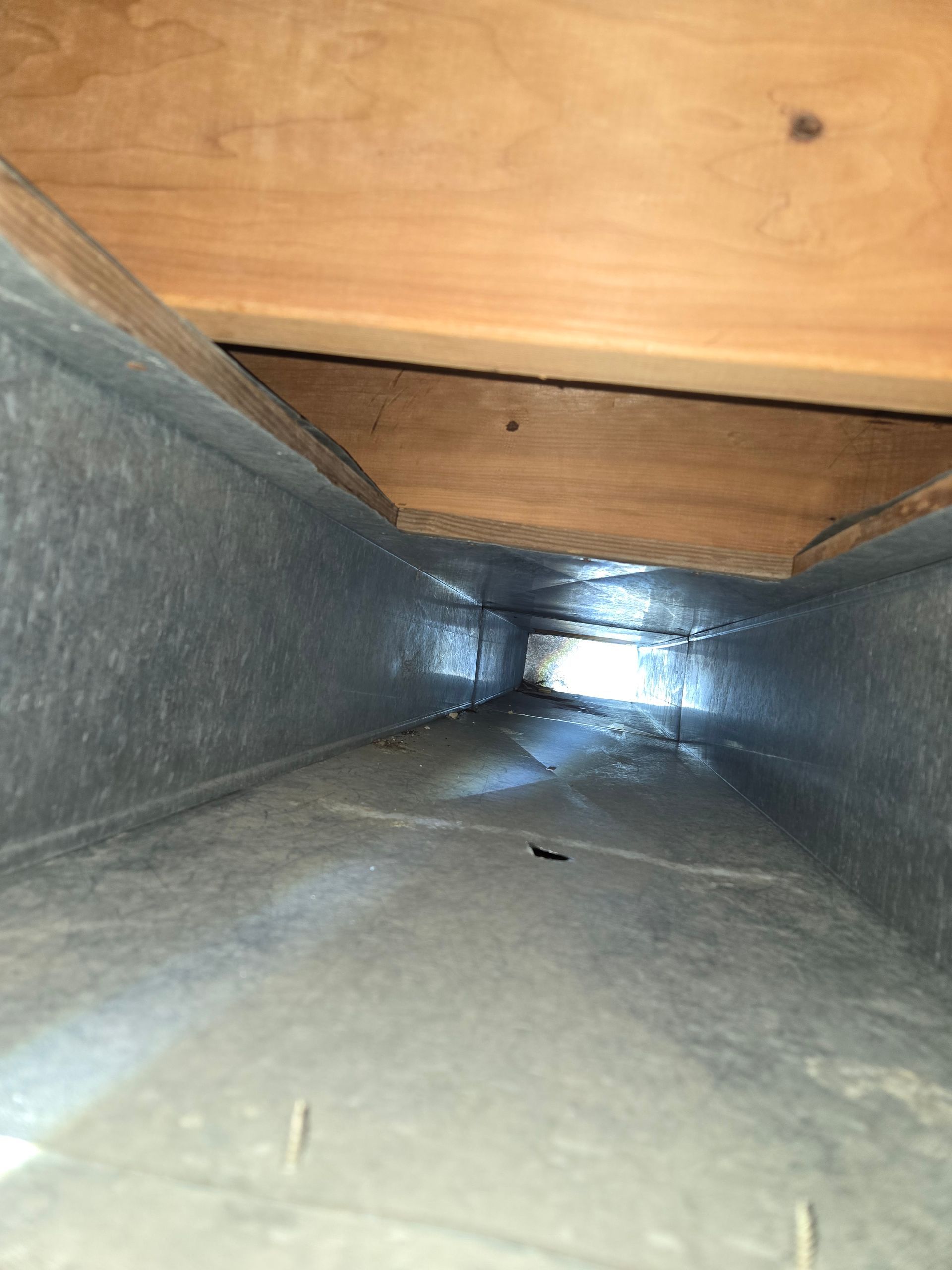 Inside view of a rectangular metal duct, showing a long, open channel, with wooden framing above.