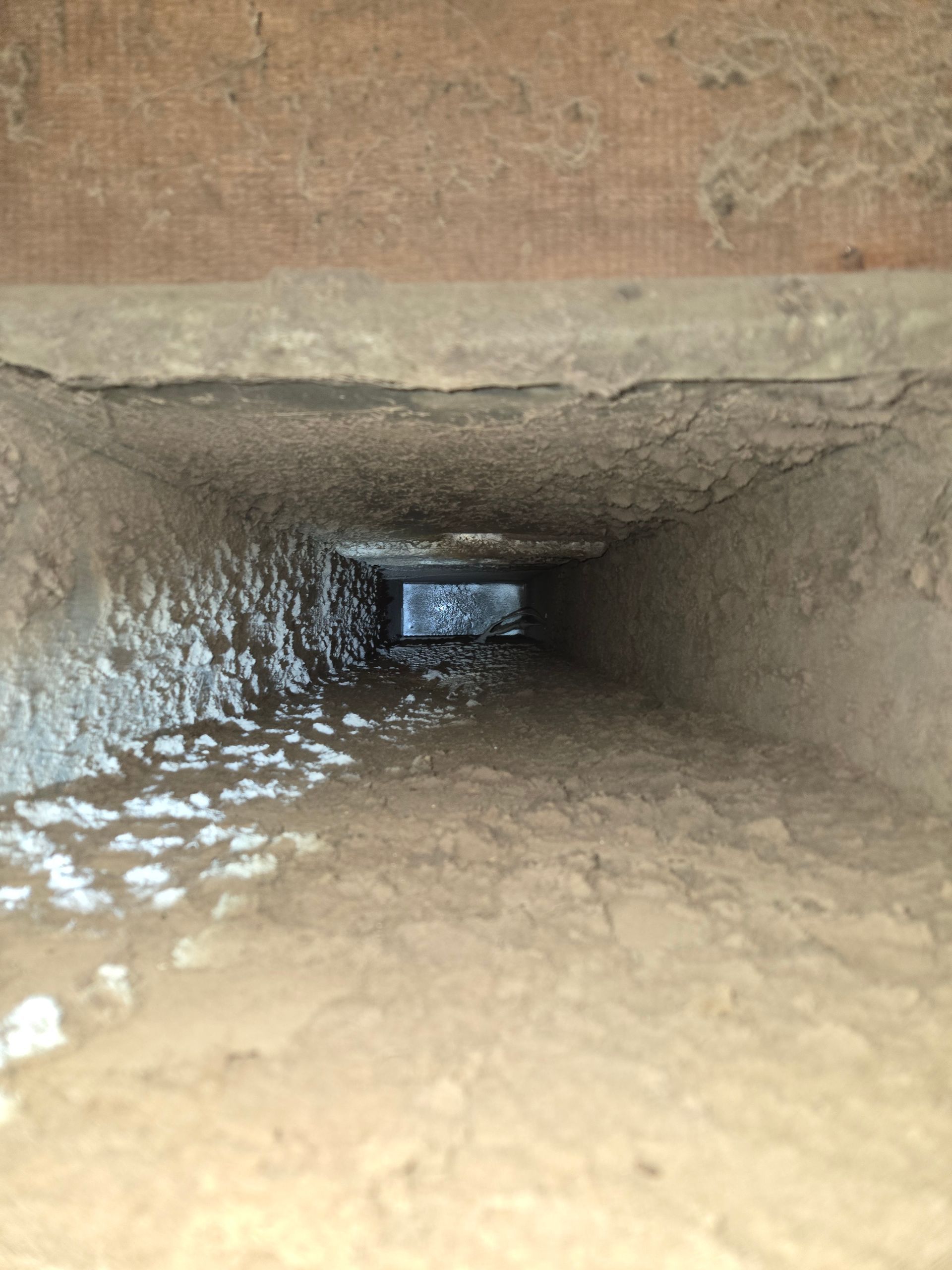 Rectangular air duct, dark and dusty, with debris visible along the sides.