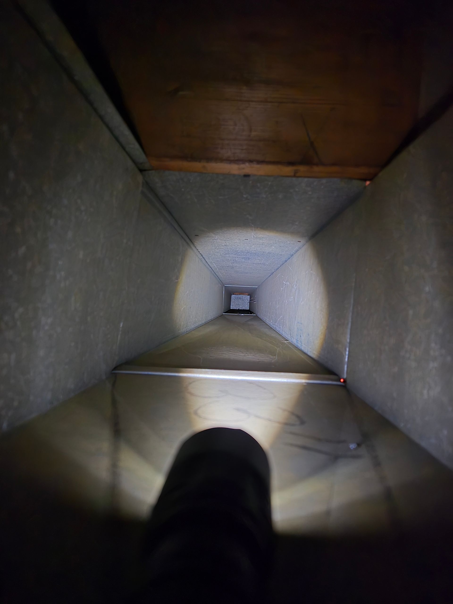 Looking down a long, rectangular air duct; flashlight illuminates the interior.