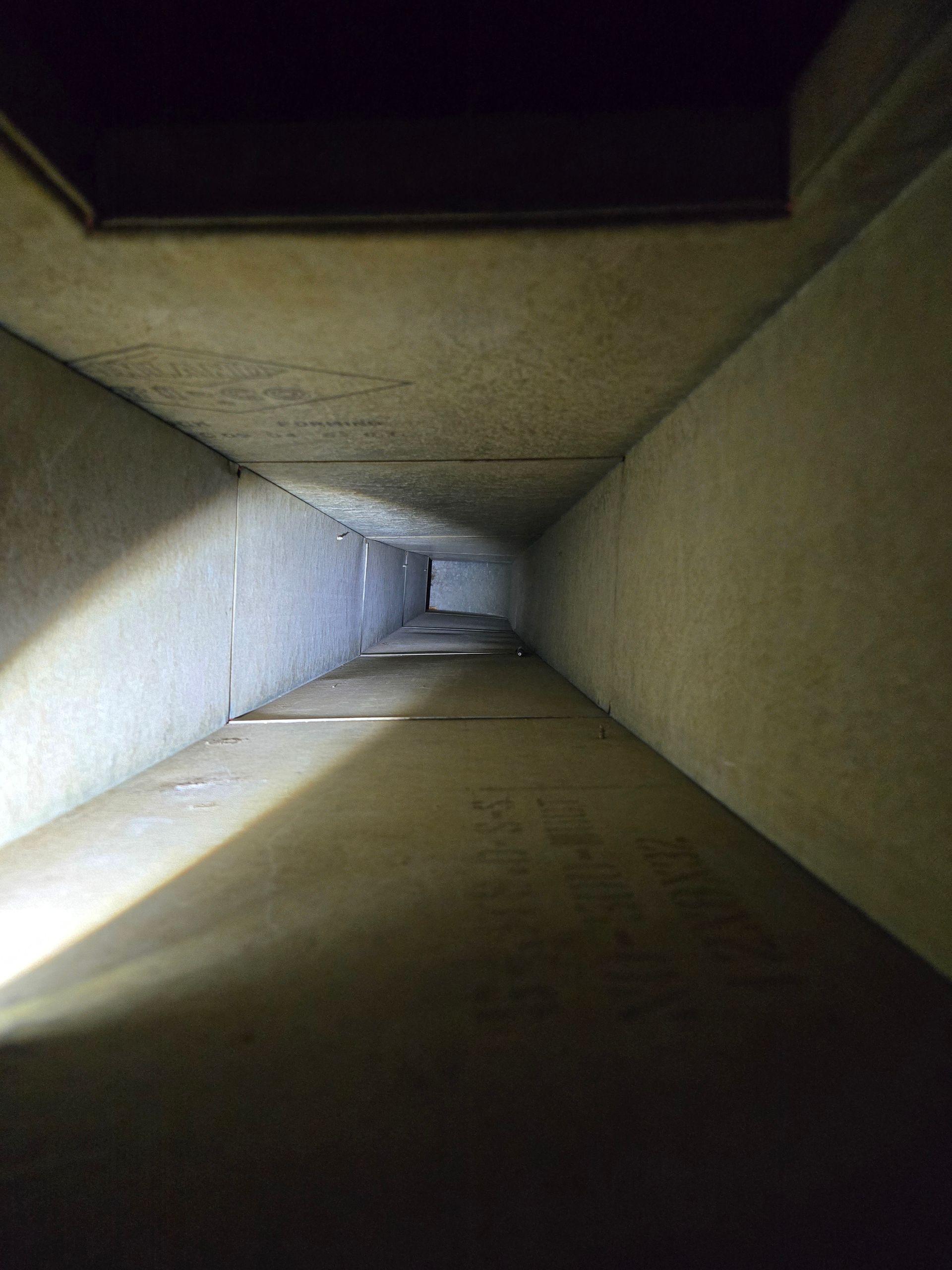 Long, narrow, concrete tunnel with a light source at the bottom, viewed from above.