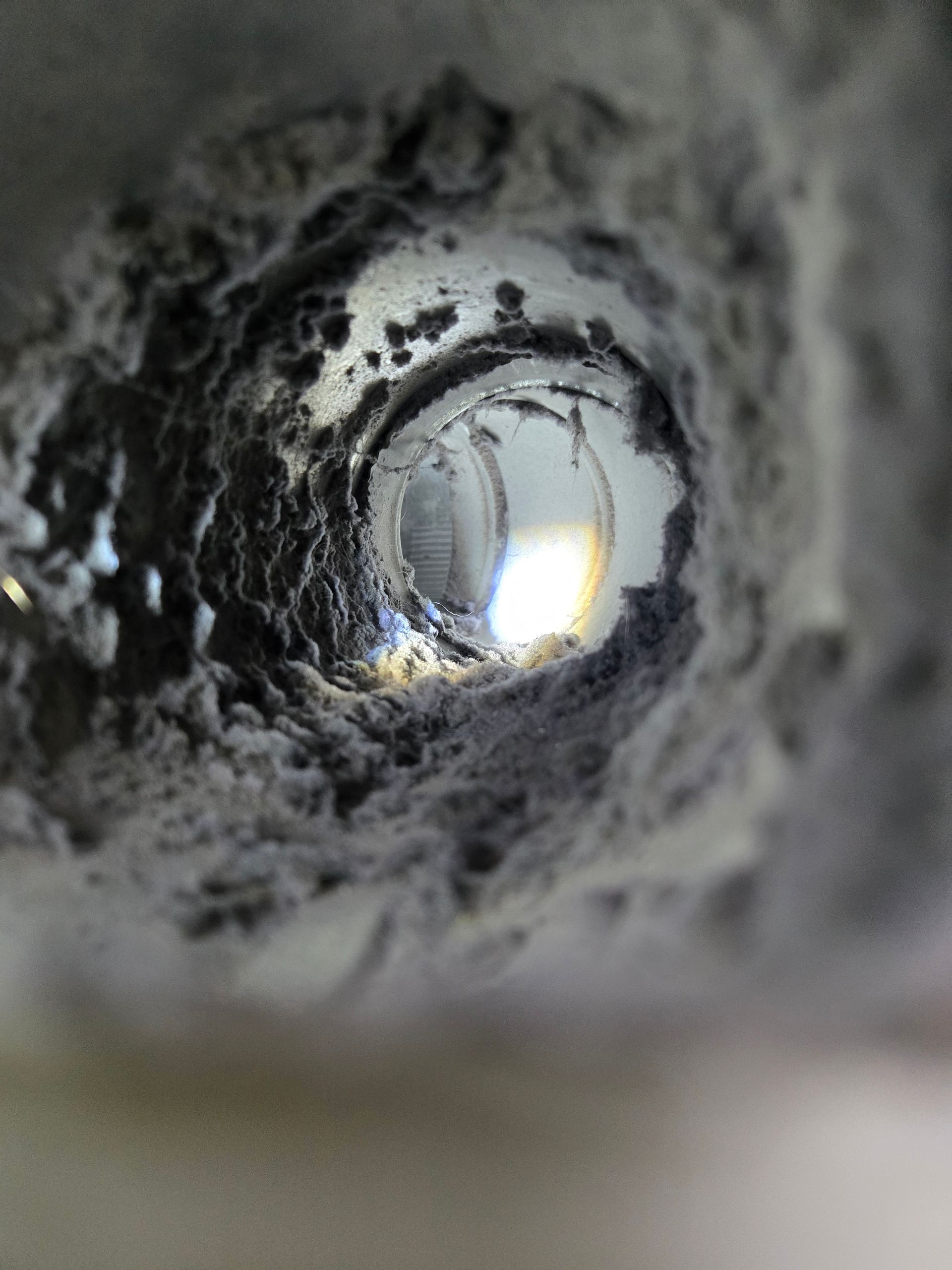 View down a dusty, gray, cylindrical pipe; a bright, blurred light source is at the end.