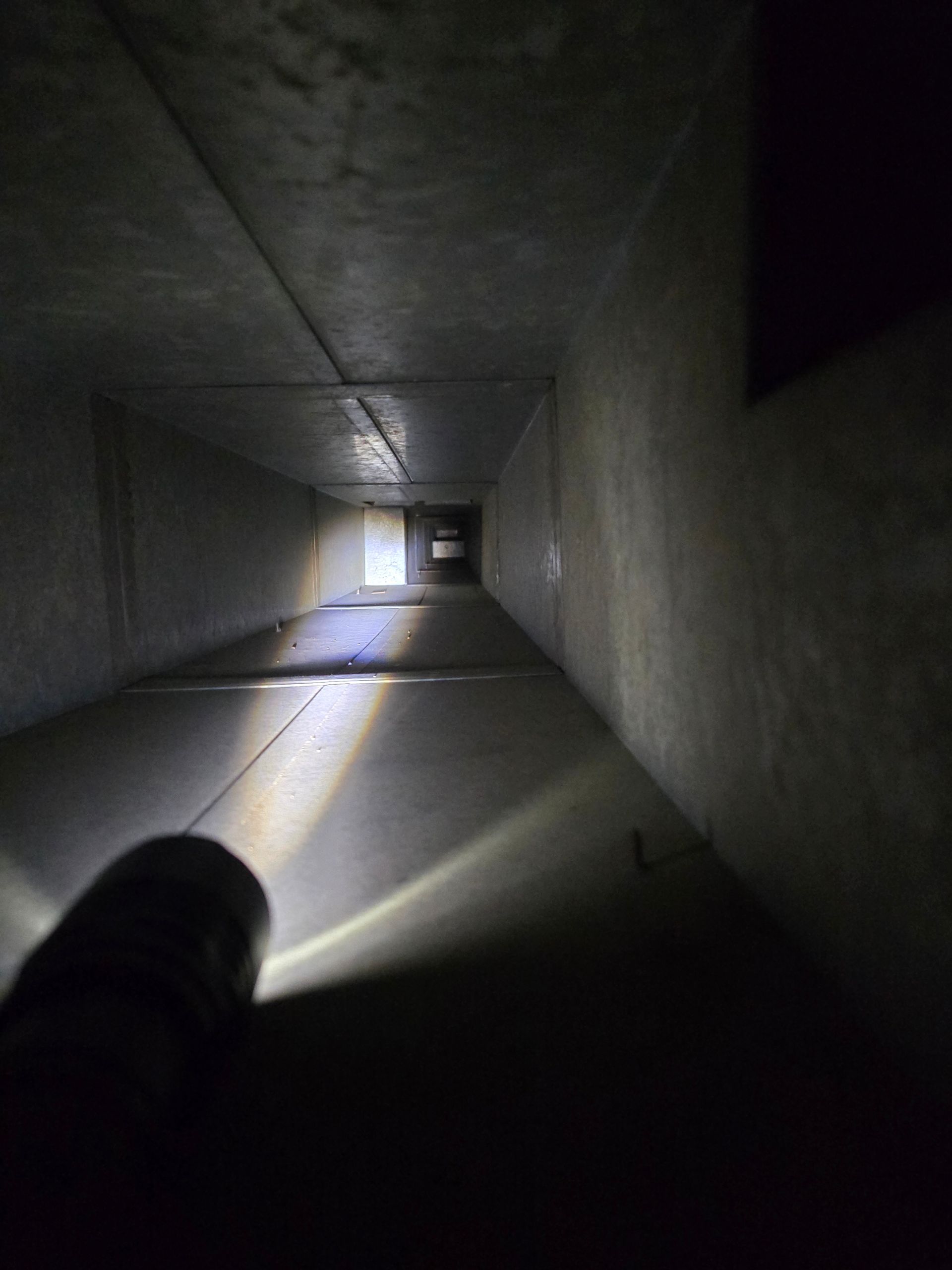 A flashlight illuminates a long, dark rectangular tunnel.