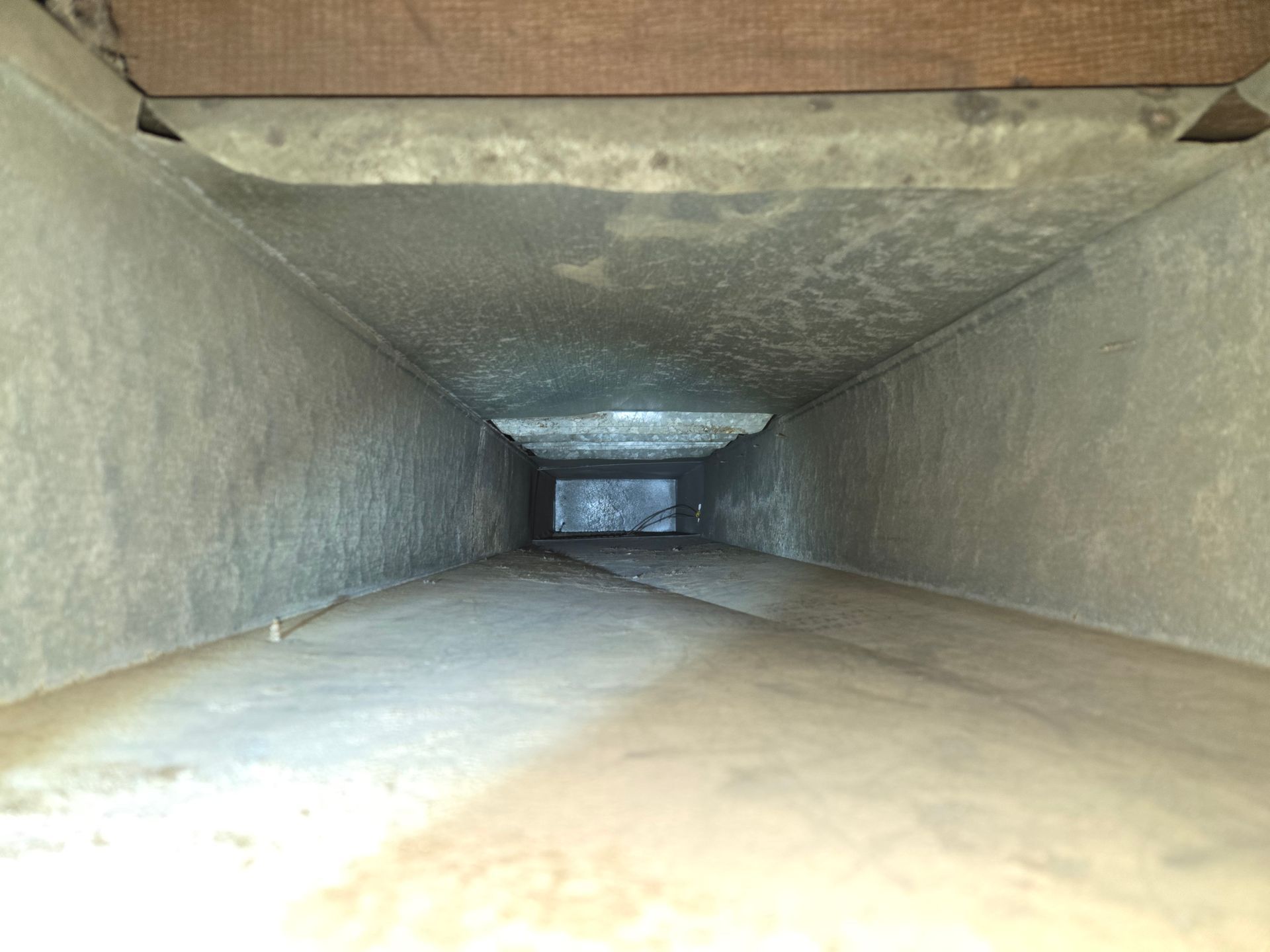 A rectangular metal HVAC duct, viewed from inside, showing dust and debris accumulation.