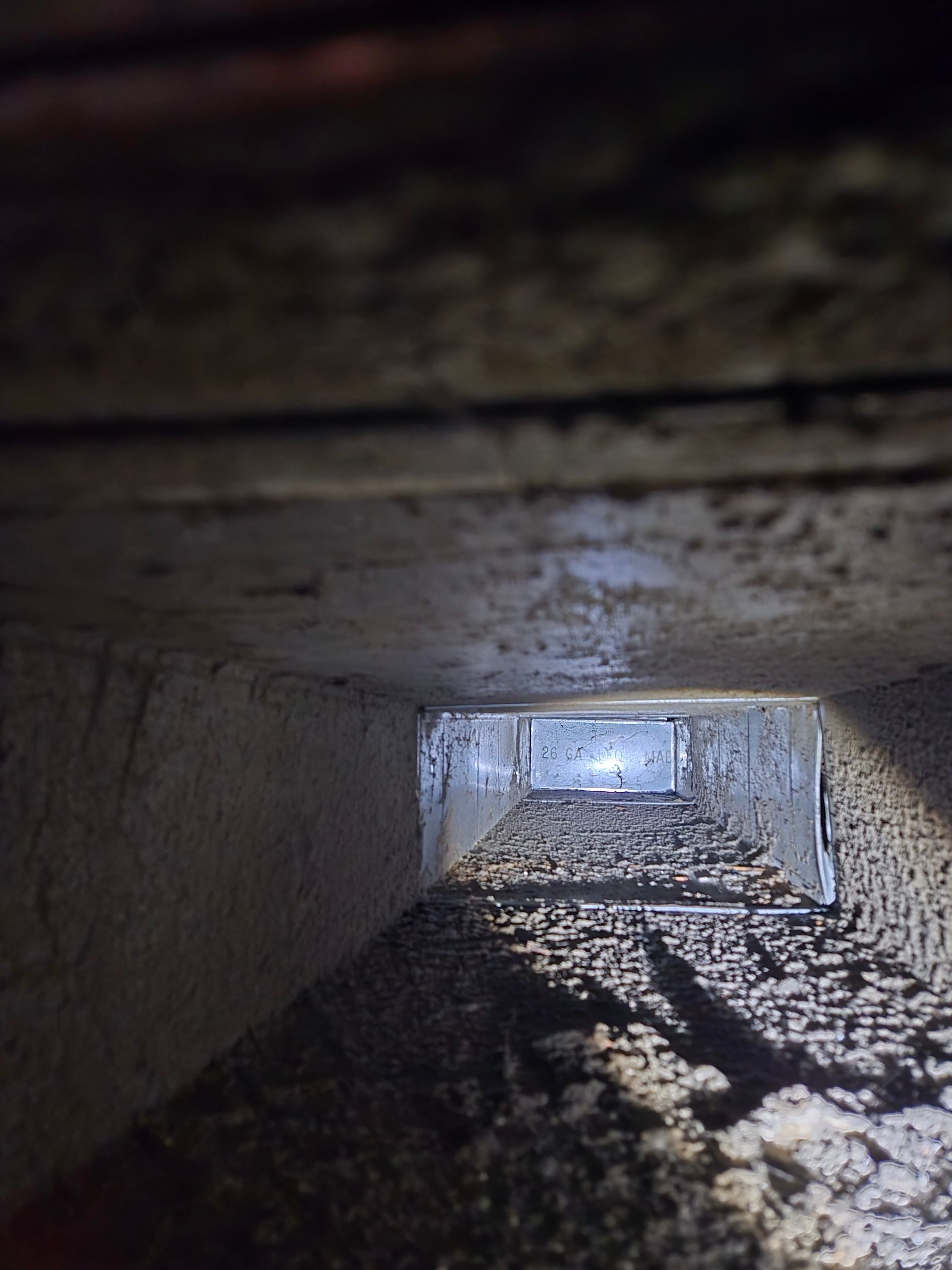Inside view of a dusty air duct with a screen at the end, appearing dark with a hint of light.