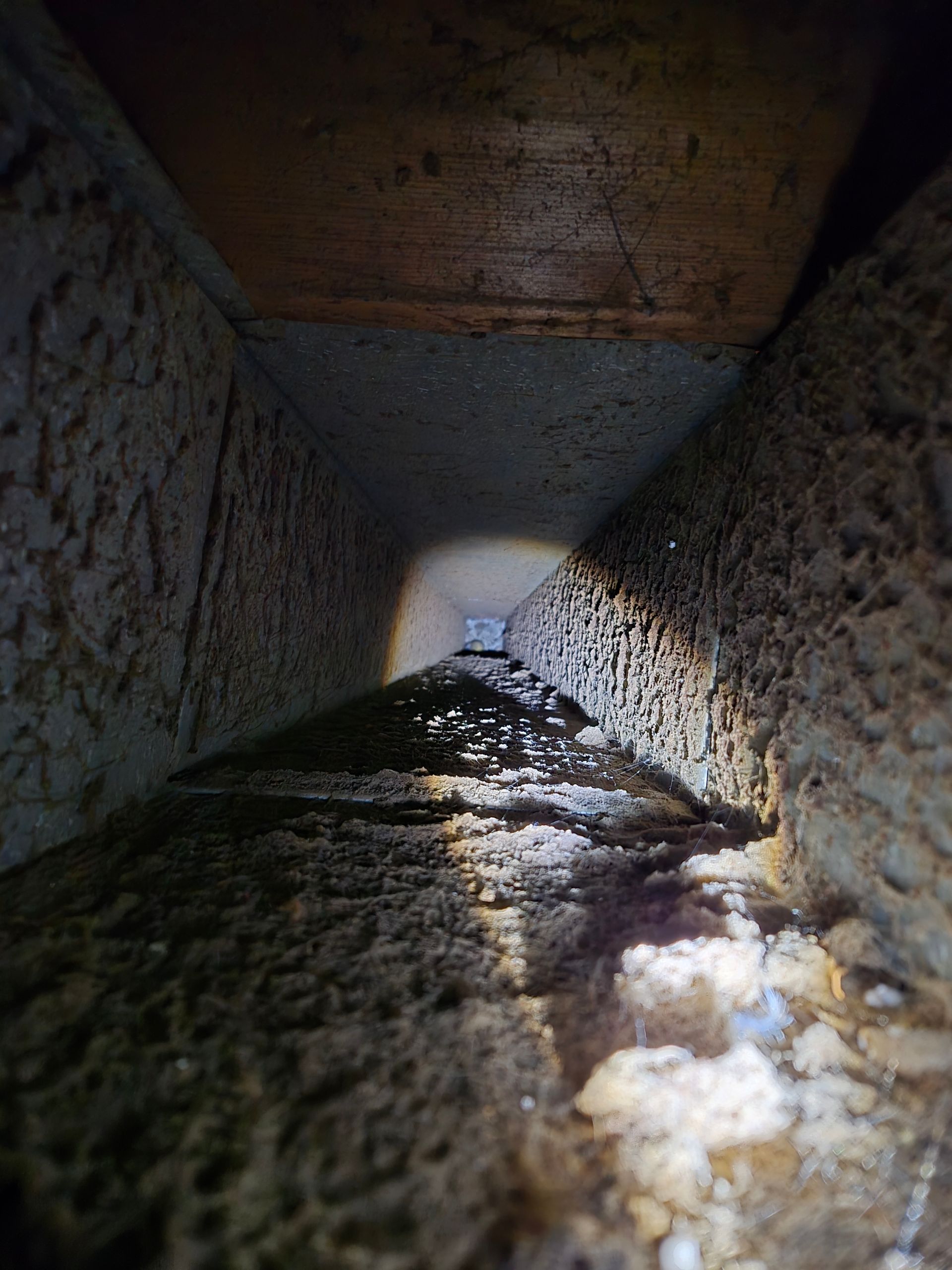 Inside of a dusty, rectangular air duct; light at the end, looking down the narrow, dirty space.