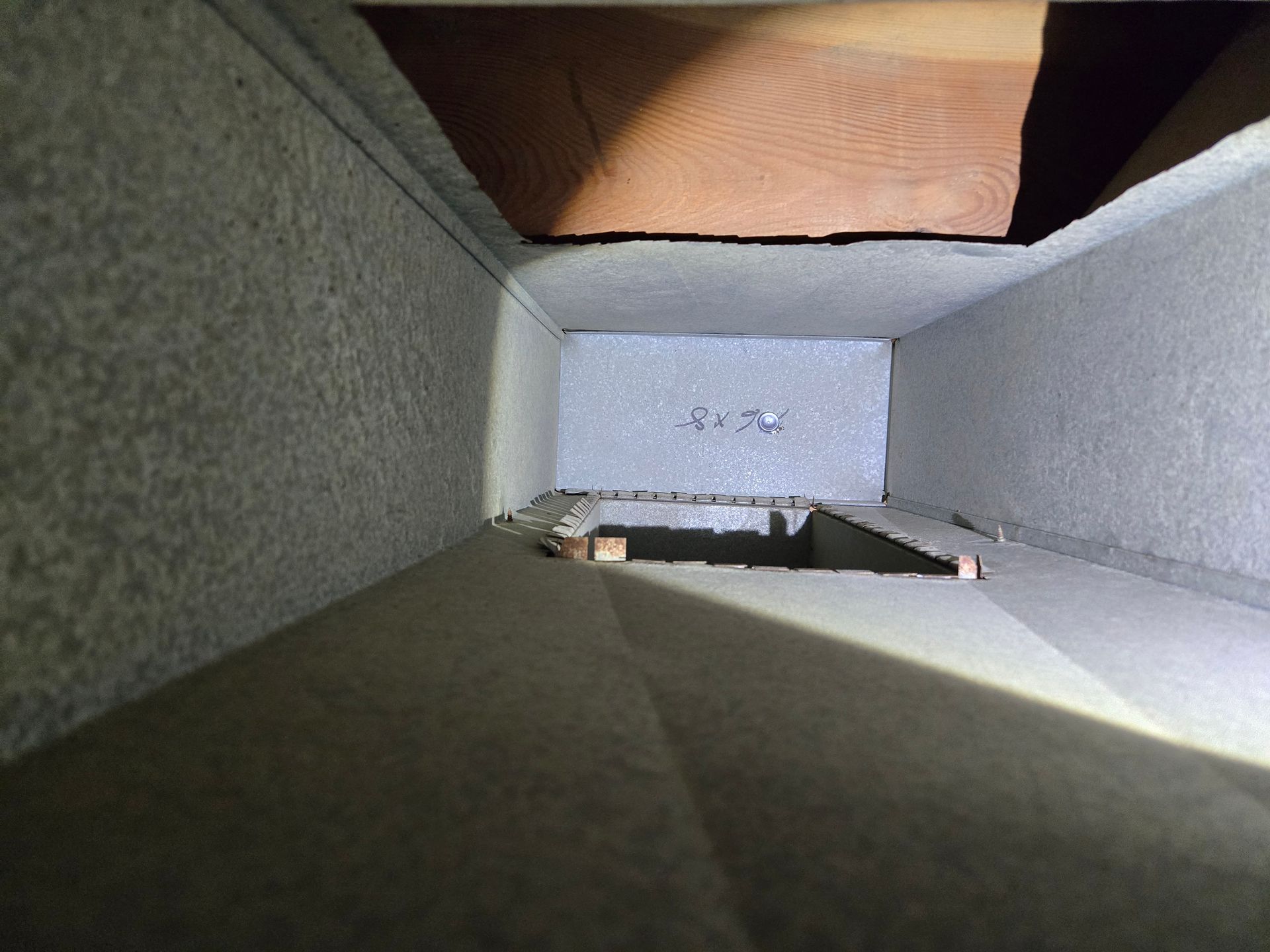 View inside a rectangular, gray-walled duct. A wooden beam is visible at the top.