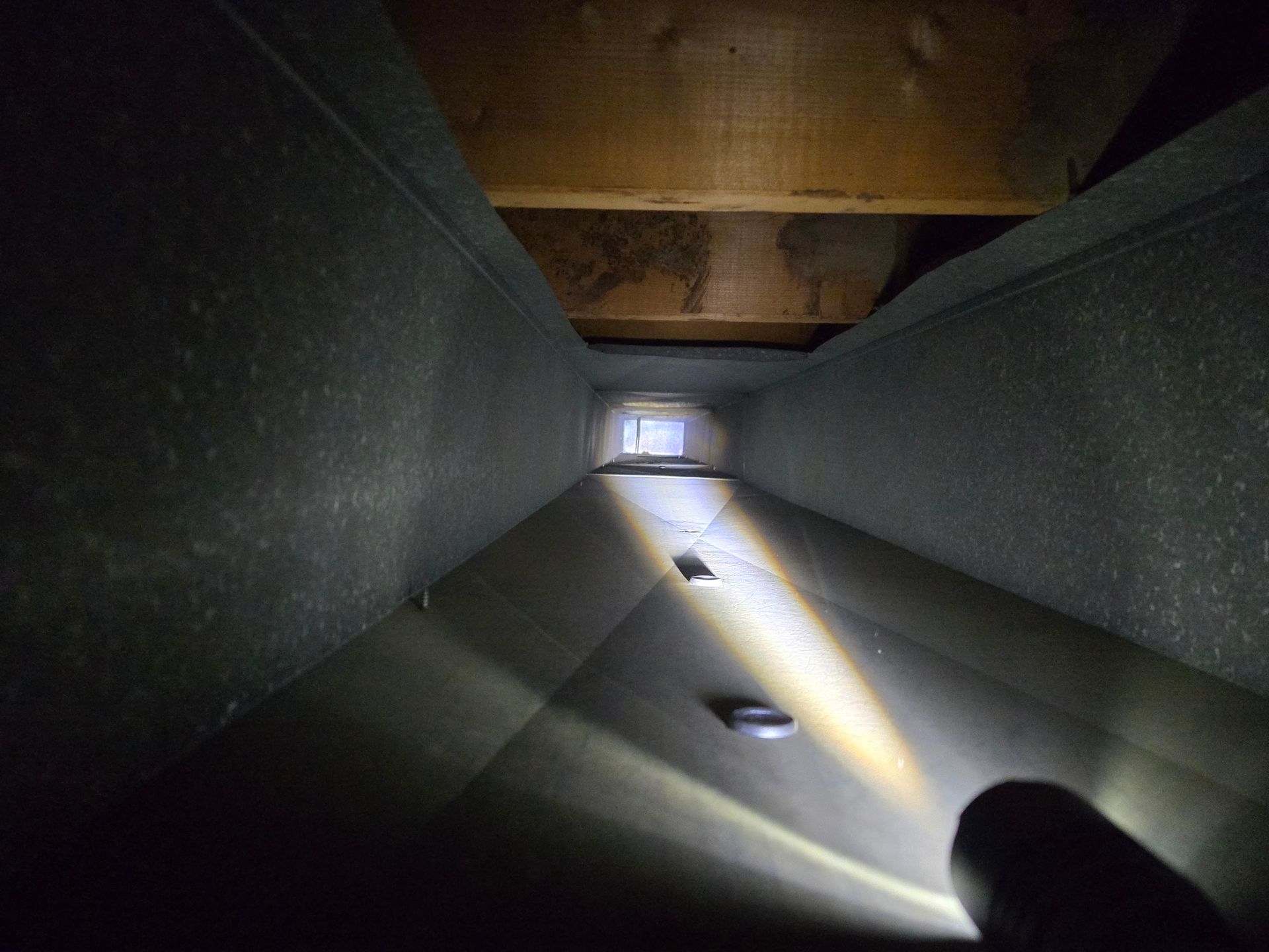 Looking down a dark duct. Bright light illuminates a rectangular opening at the end.