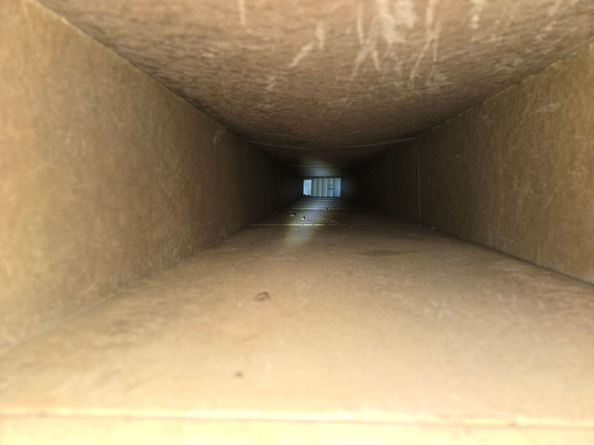 Interior view of a rectangular, dusty duct, gradually narrowing into darkness.