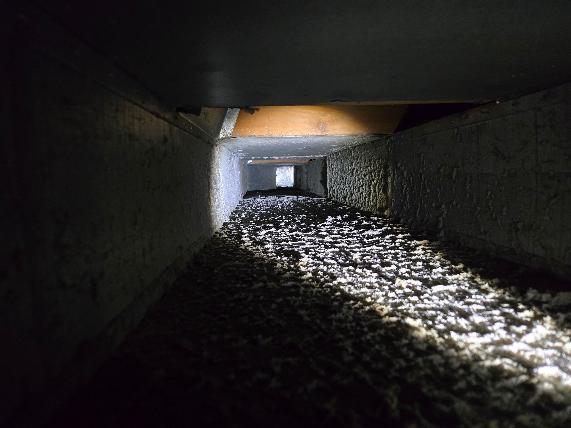 Inside view of a rectangular air duct filled with a layer of white, fibrous material, dimly lit.