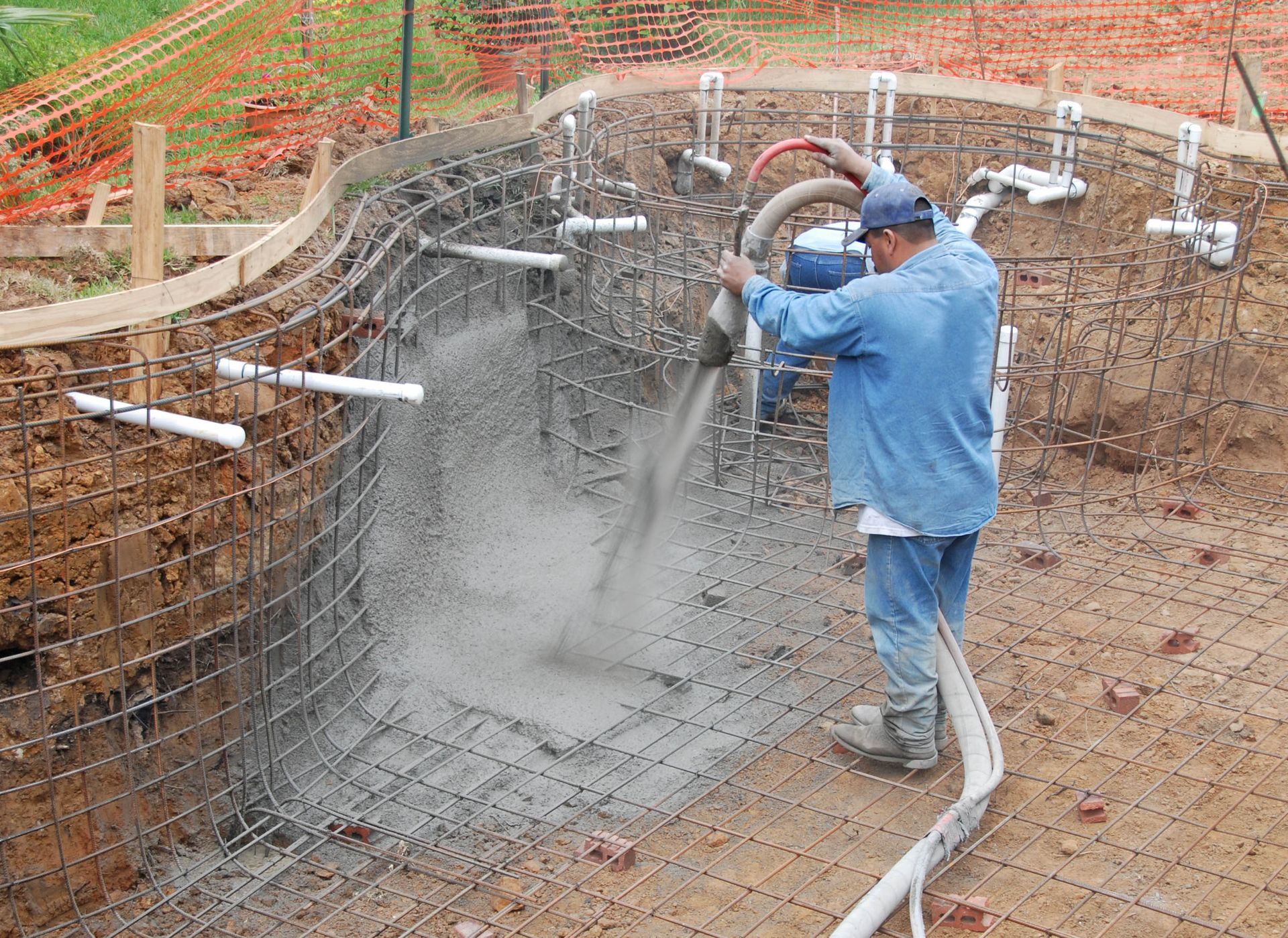 Worker spraying concrete into a rebar foundation pit at a construction site
