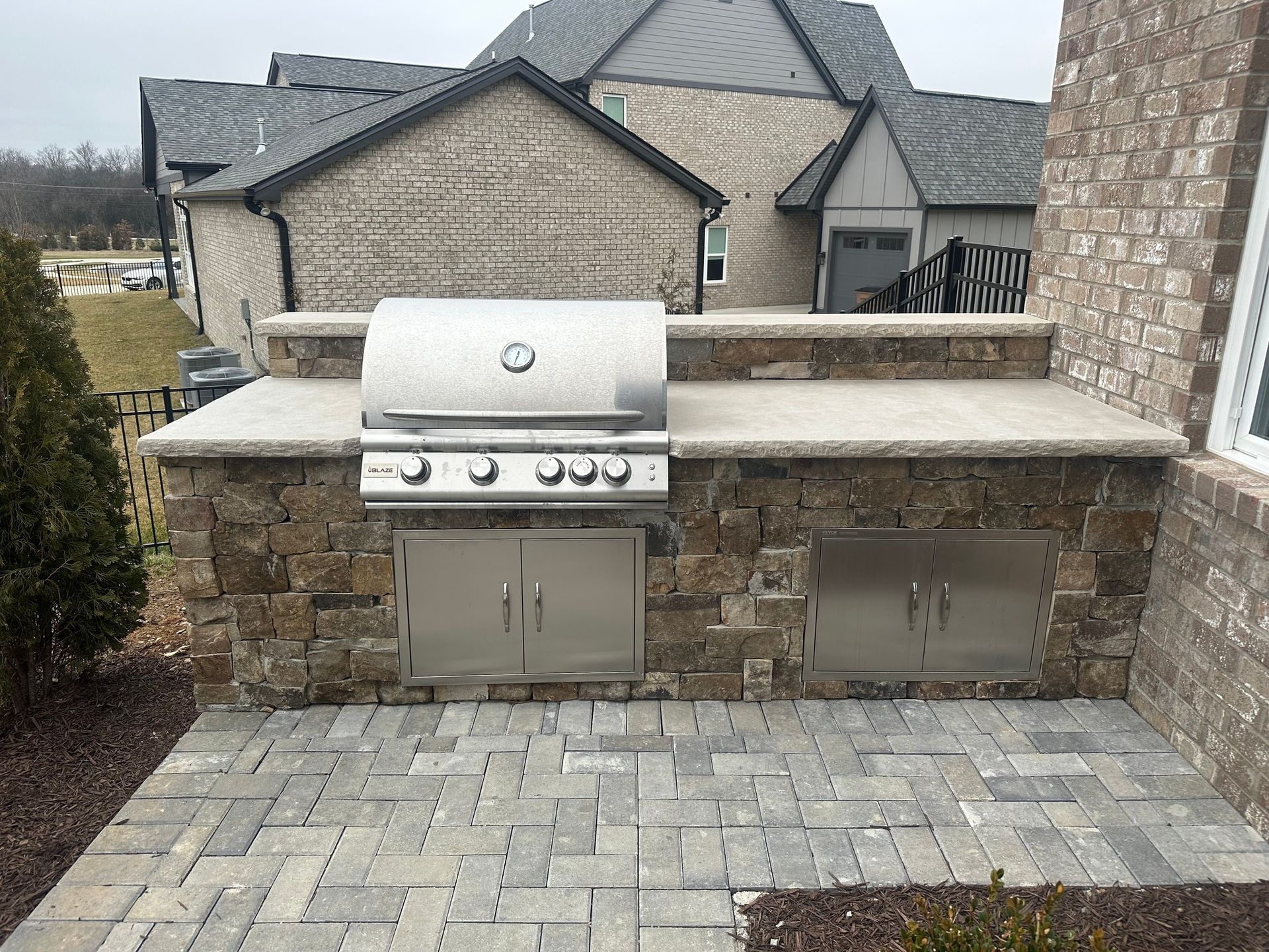 Outdoor stone patio with built-in stainless steel grill and countertop in a suburban backyard