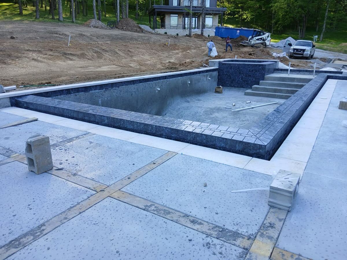 Rectangular concrete pool under construction, lined with dark tile and surrounded by a paved deck