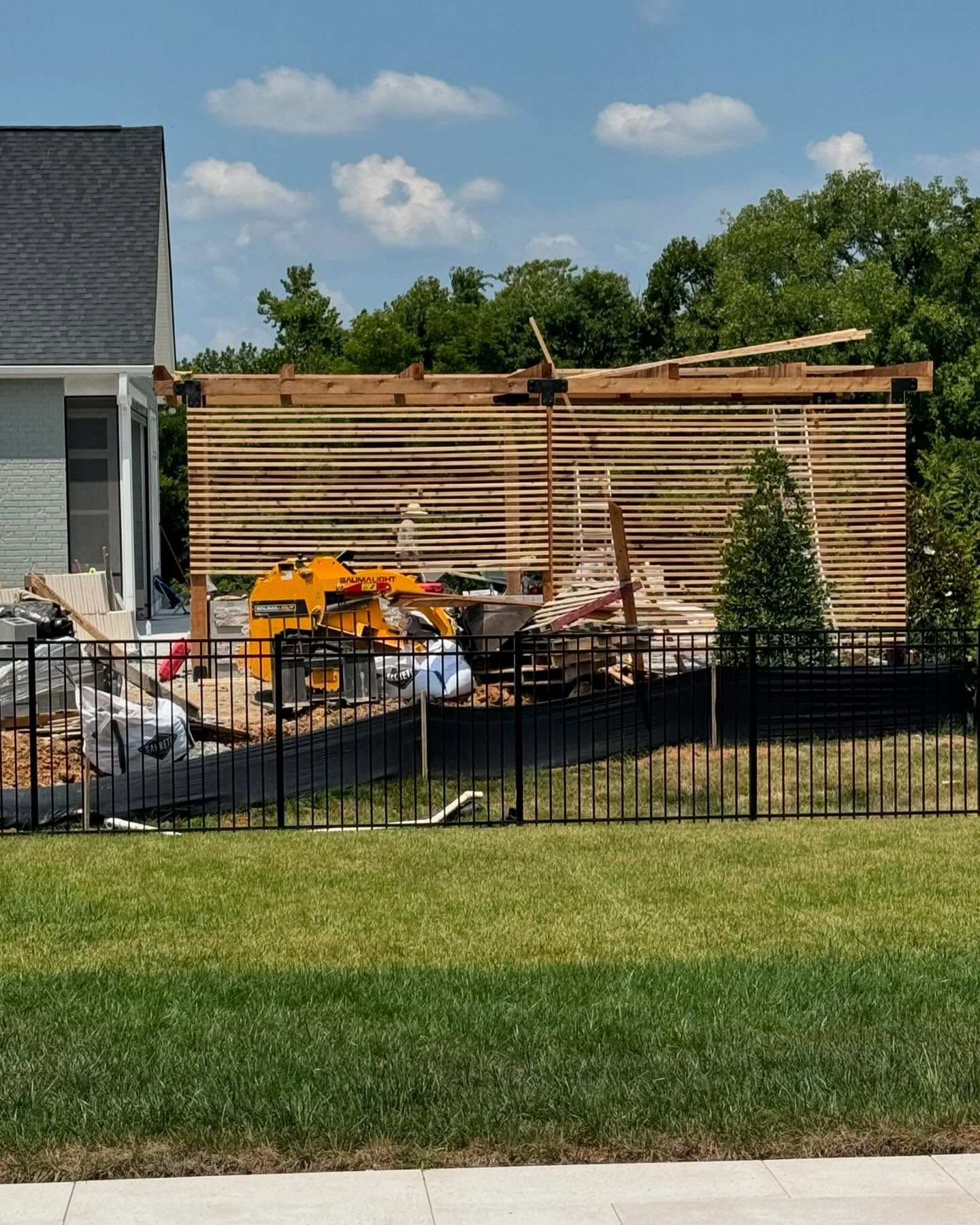 Backyard with stacked lumber, construction materials, and a black fence beside a house