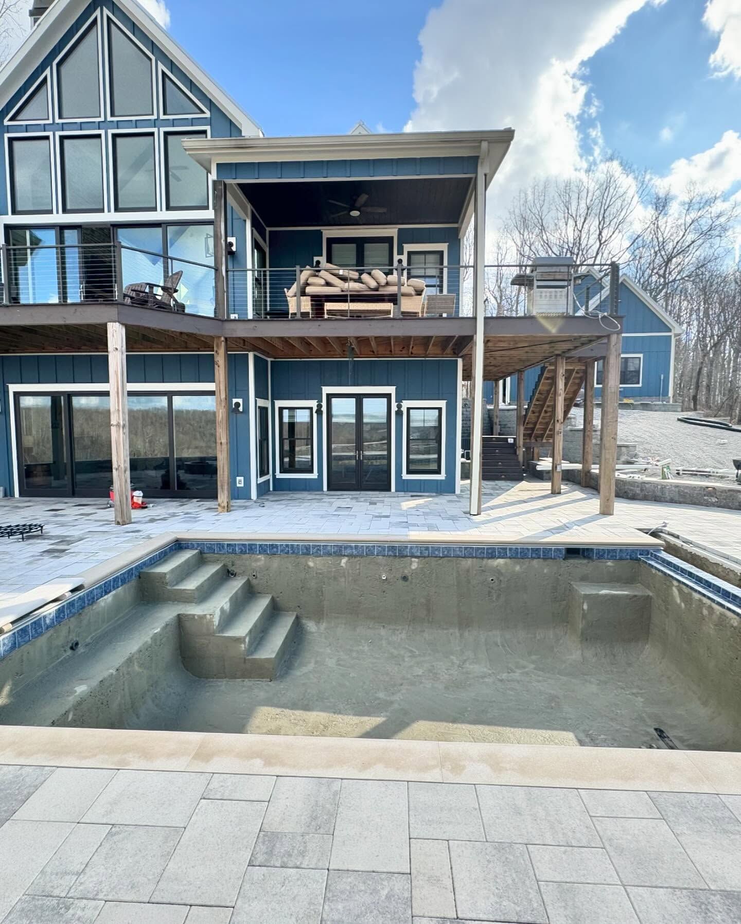Modern house with empty rectangular pool and patio, reflecting windows under a partly cloudy sky