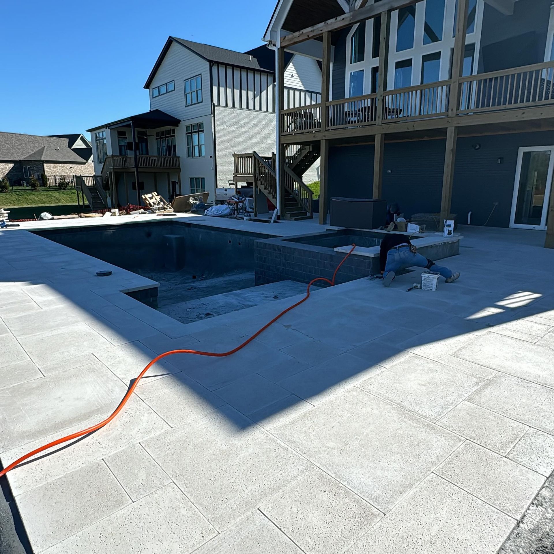 Backyard with a partially finished in-ground pool beside a house, with workers using a hose and equipment.