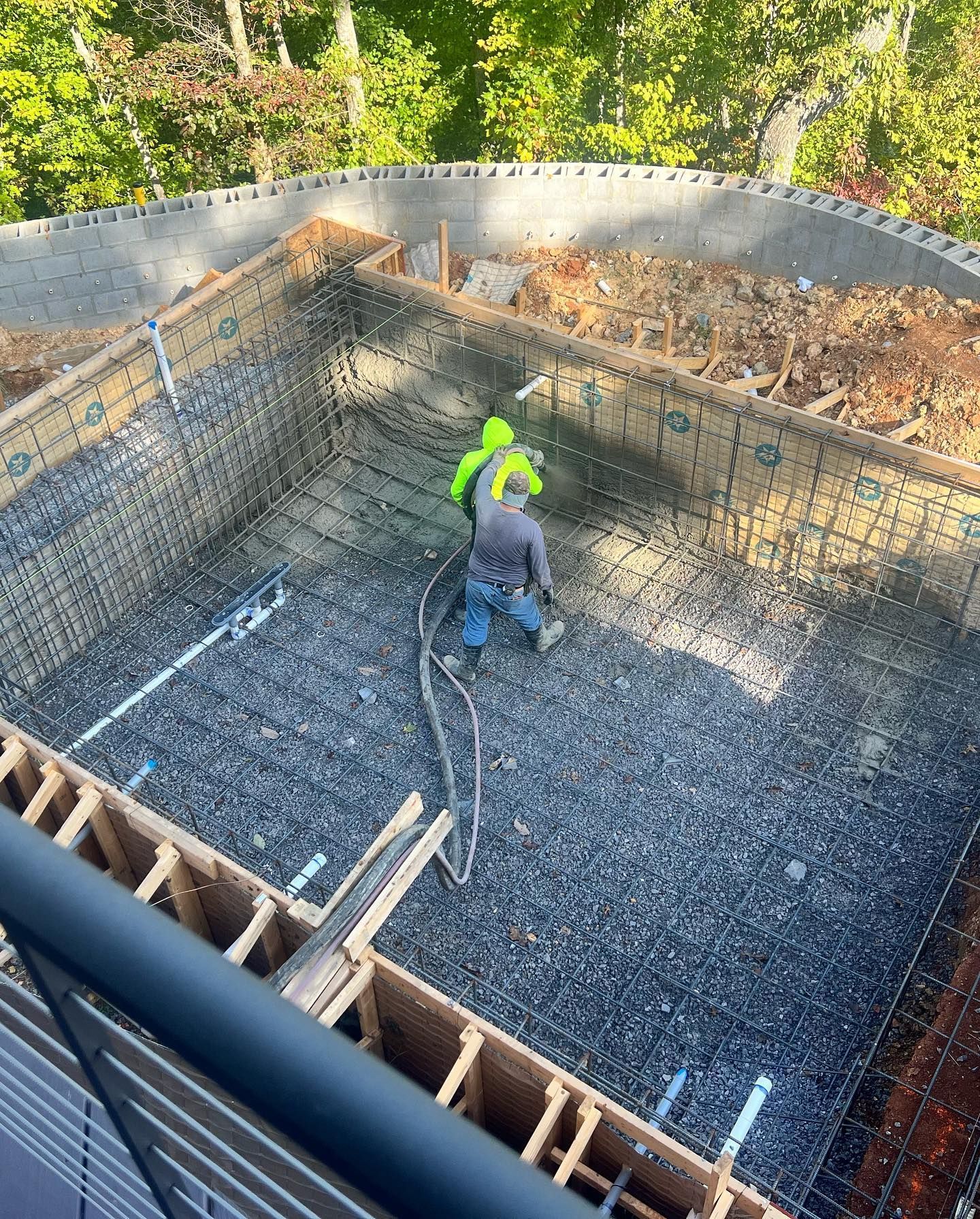 Worker in neon green jacket in a large concrete foundation pit with rebar and gravel, viewed from above