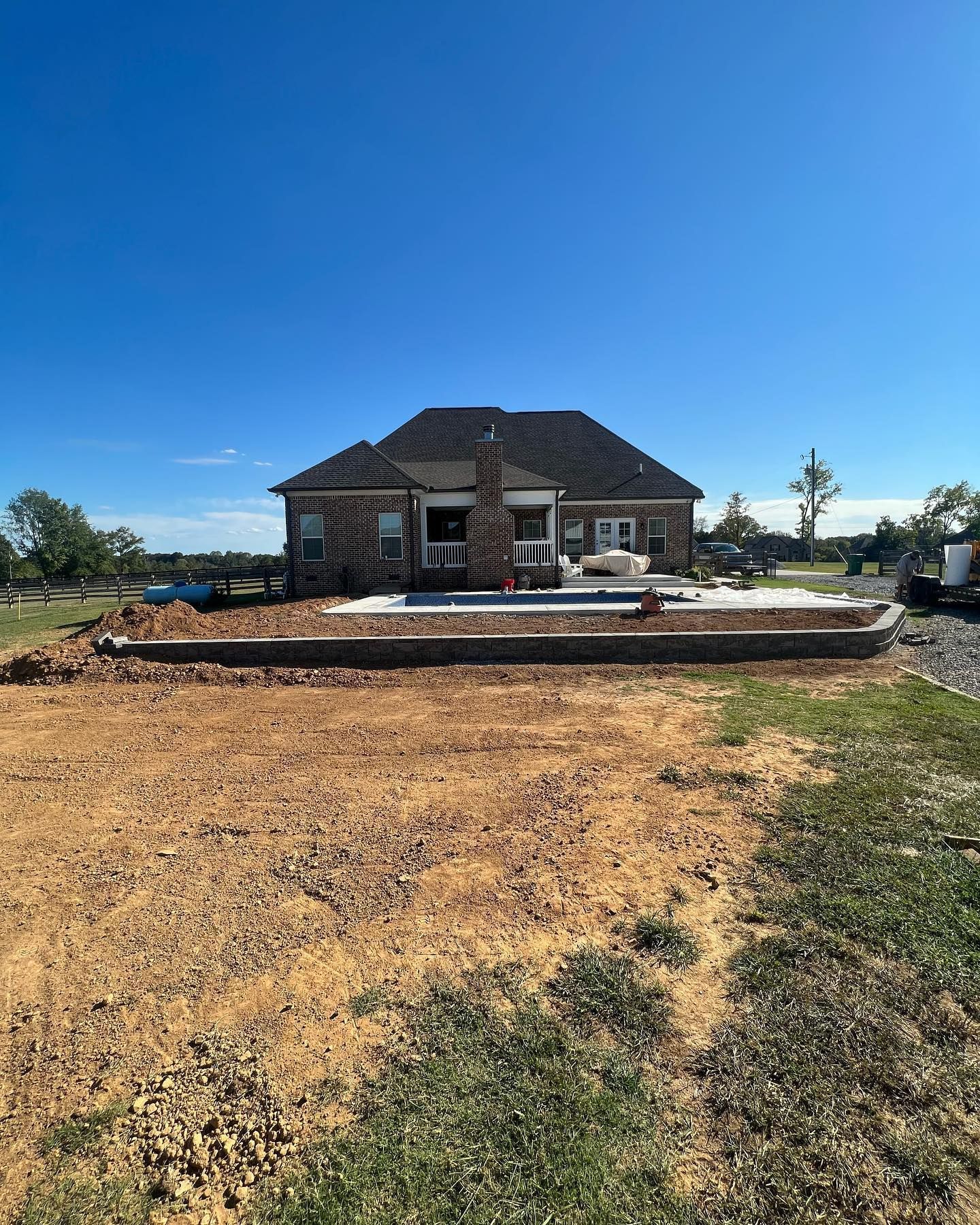 Stone house under construction on a sunny lot with dirt foreground and blue sky