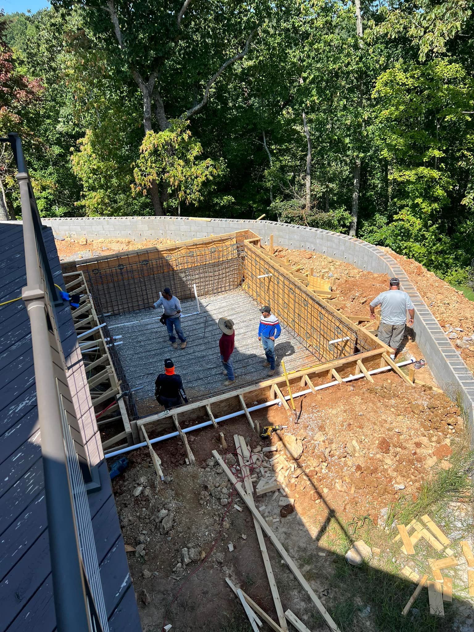 Workers building a house foundation with wooden forms and rebar in a wooded backyard