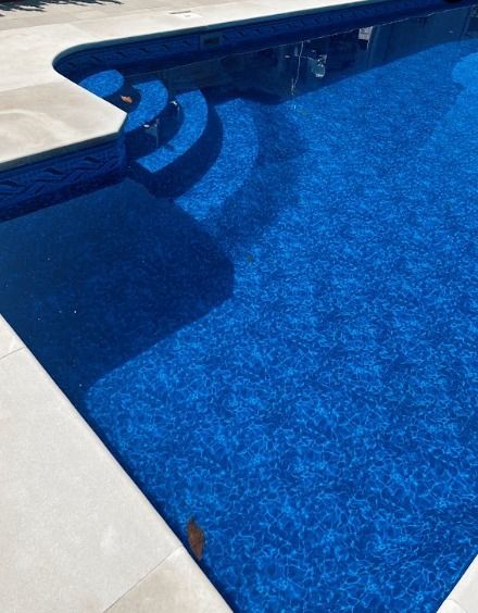 Blue swimming pool with steps and white deck edge in bright sunlight