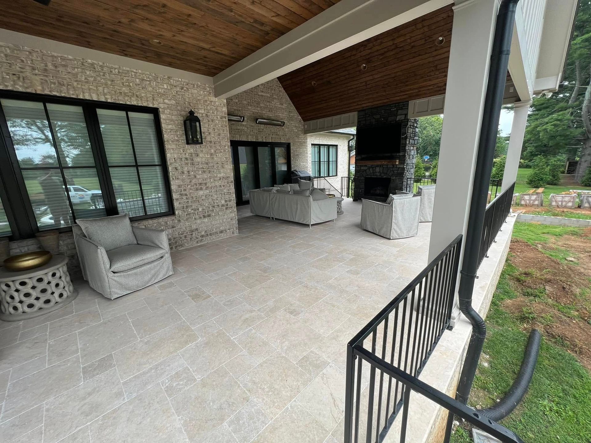 Covered patio with wicker chairs and a dark wood ceiling, overlooking a landscaped yard.