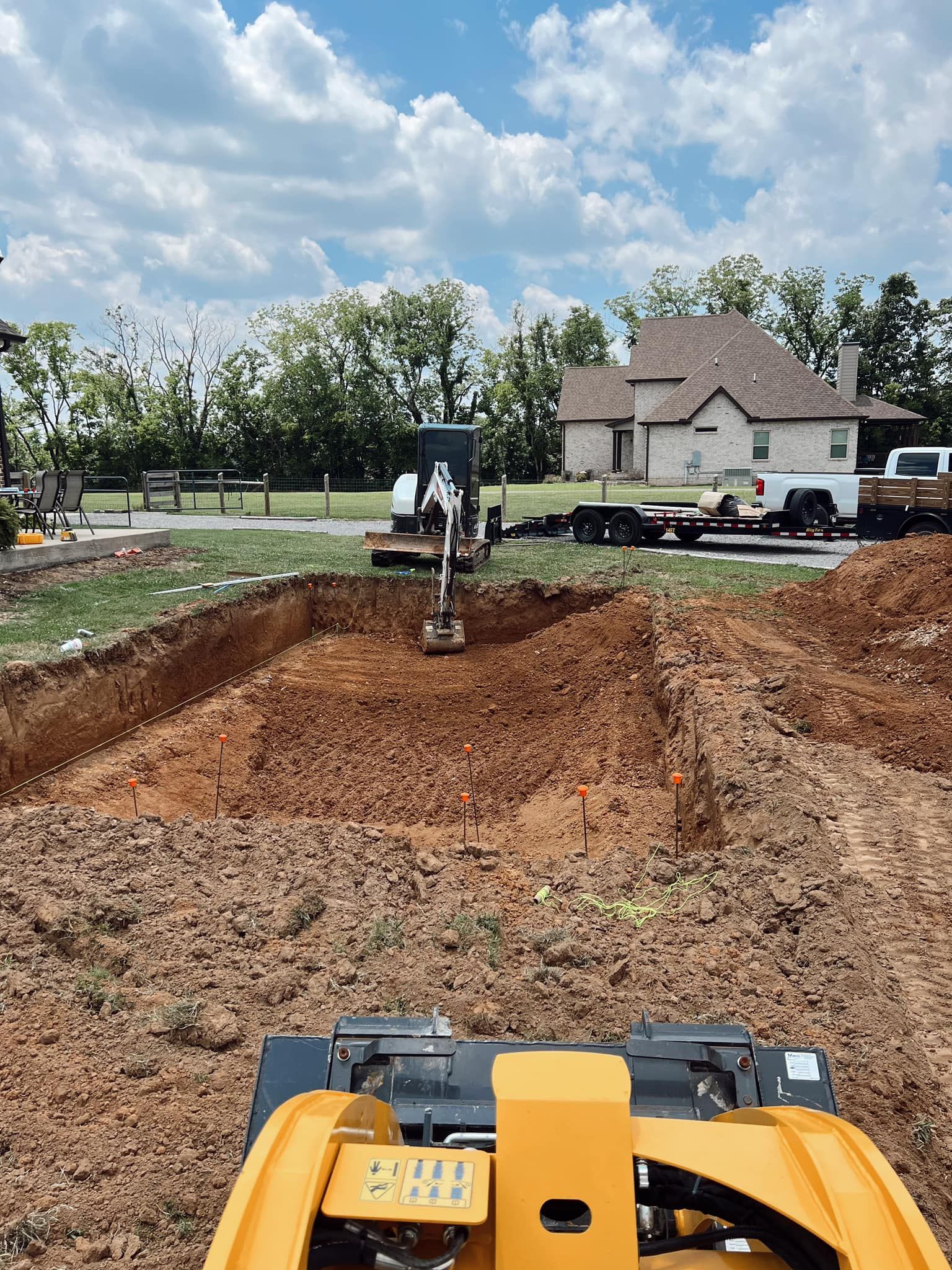 Construction site with excavated dirt pit and yellow excavator in foreground under cloudy sky