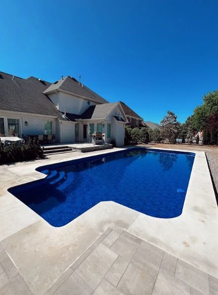Backyard swimming pool beside a large house under a clear blue sky