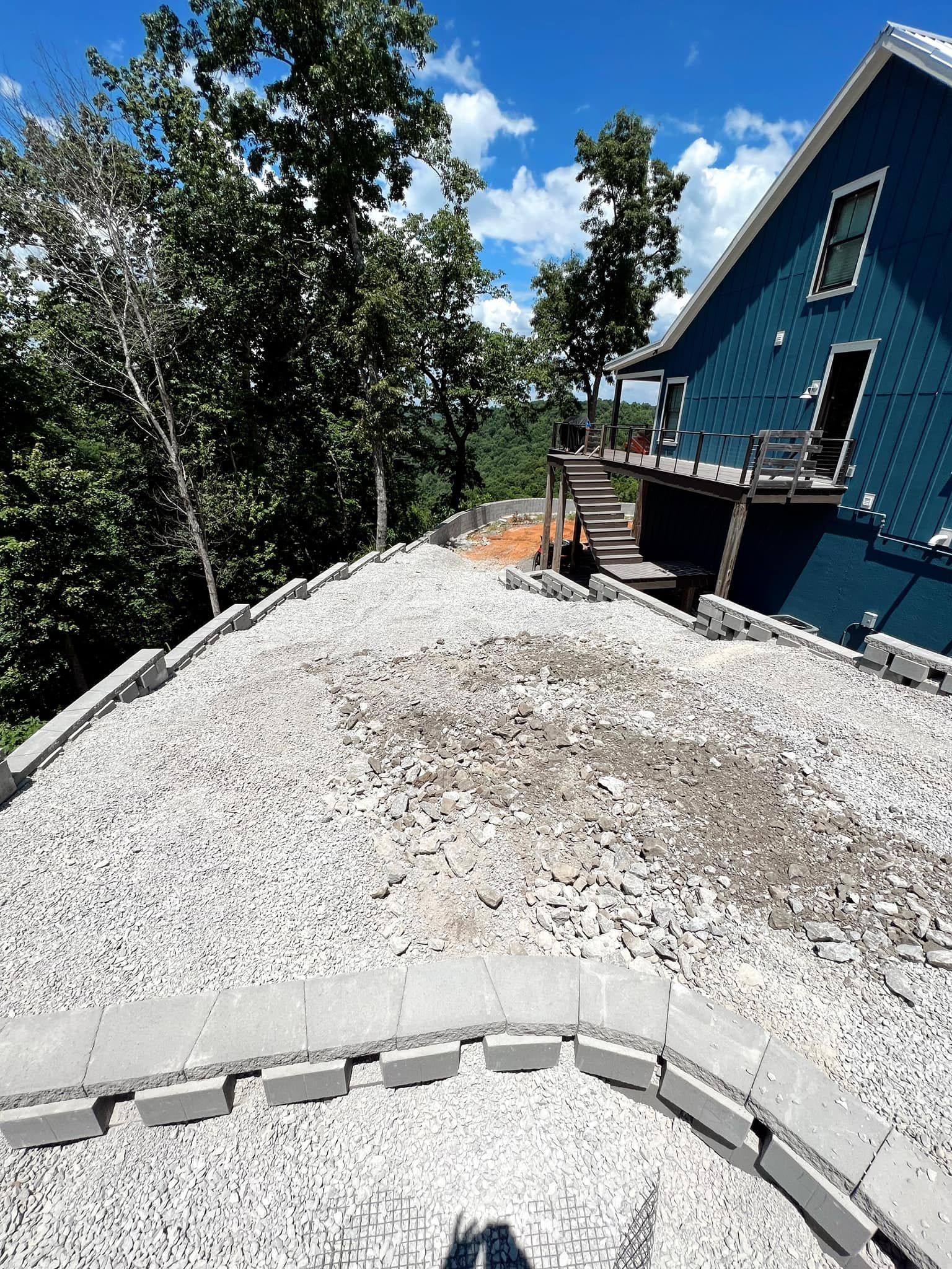 Gravel-covered yard beside a blue house and deck, with trees and blue sky in the background