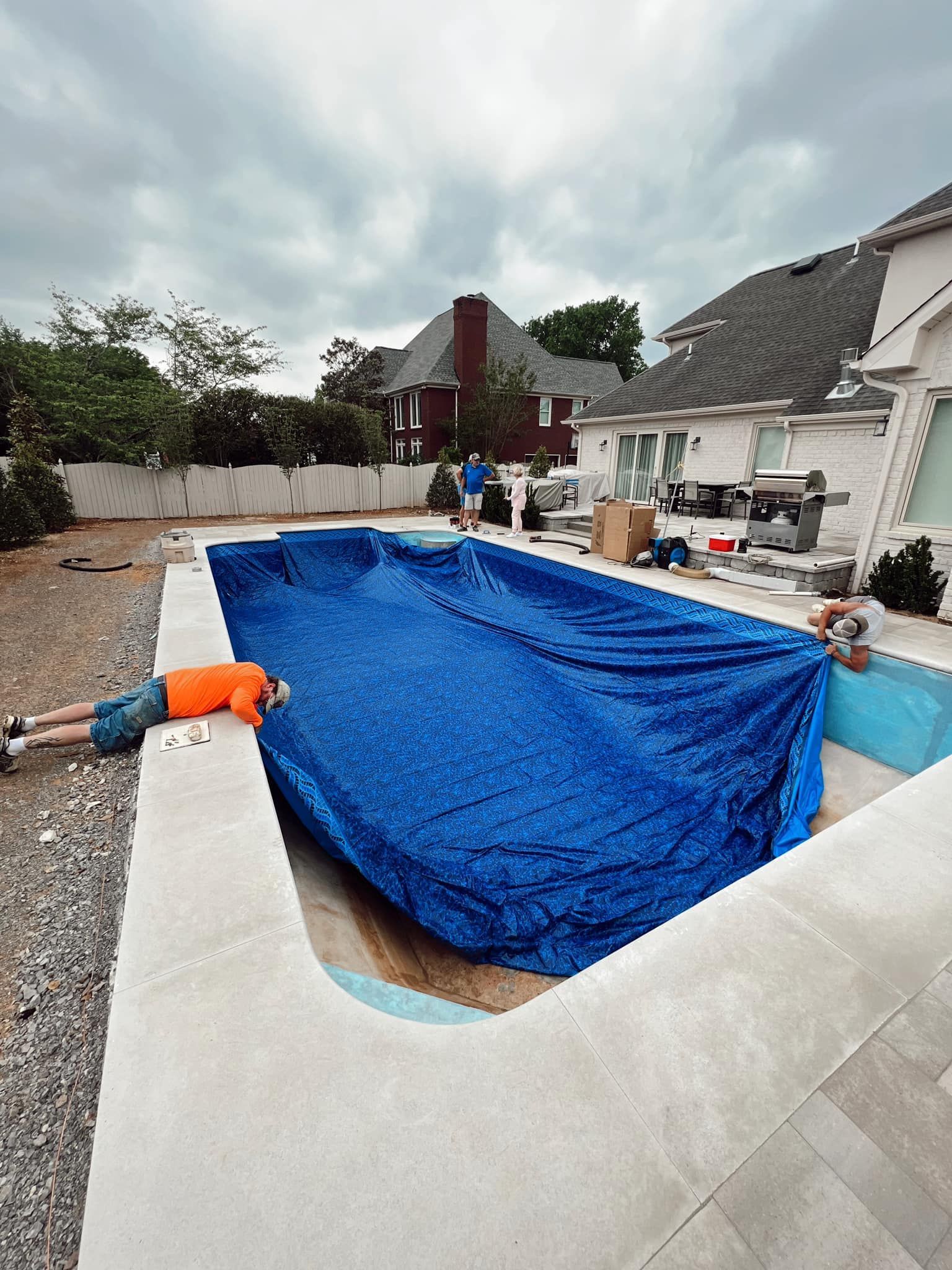 Backyard swimming pool under construction, lined with blue tarp and surrounded by workers and tools
