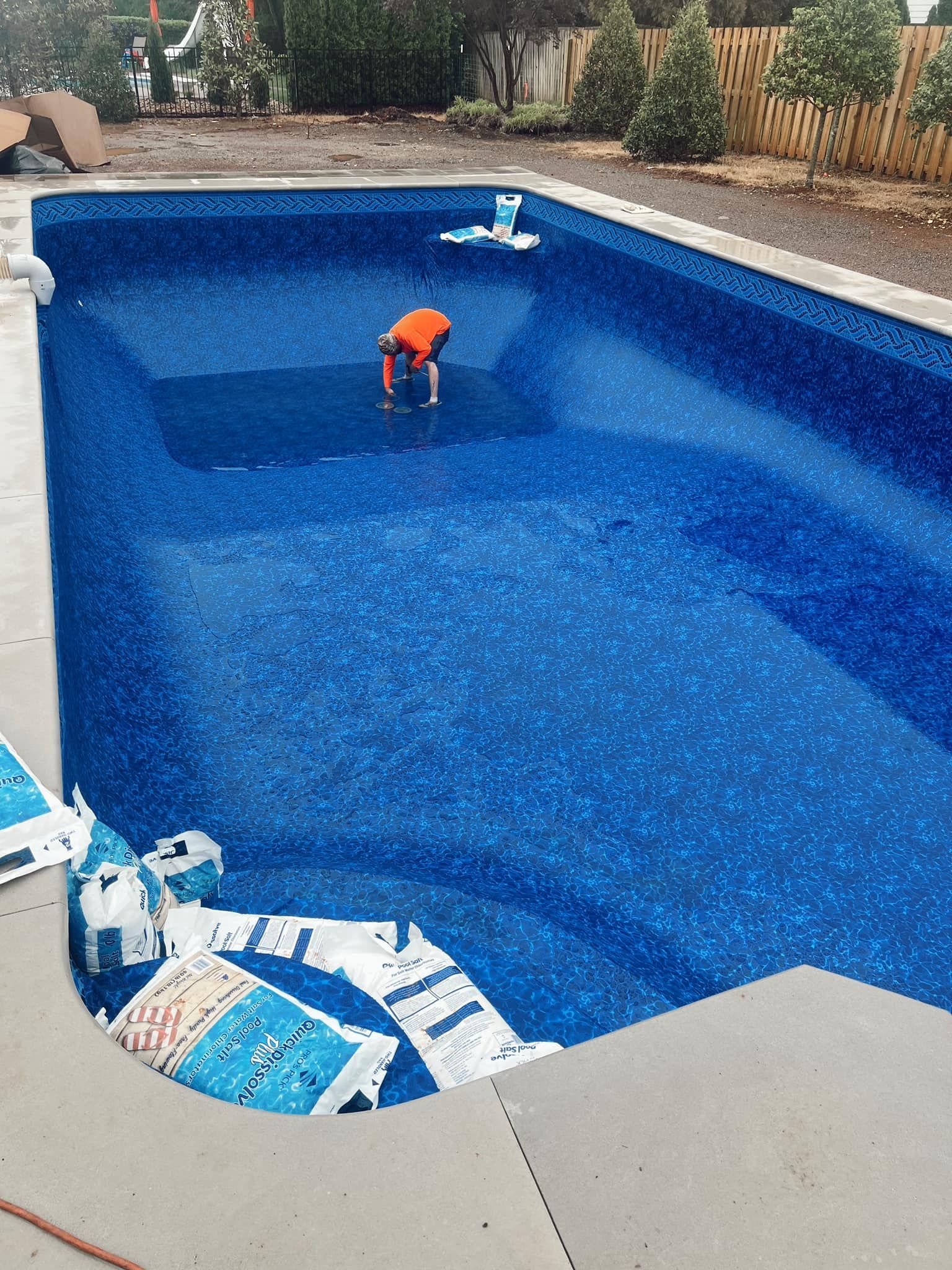 Small child in an orange shirt standing in an empty blue swimming pool during cleaning.
