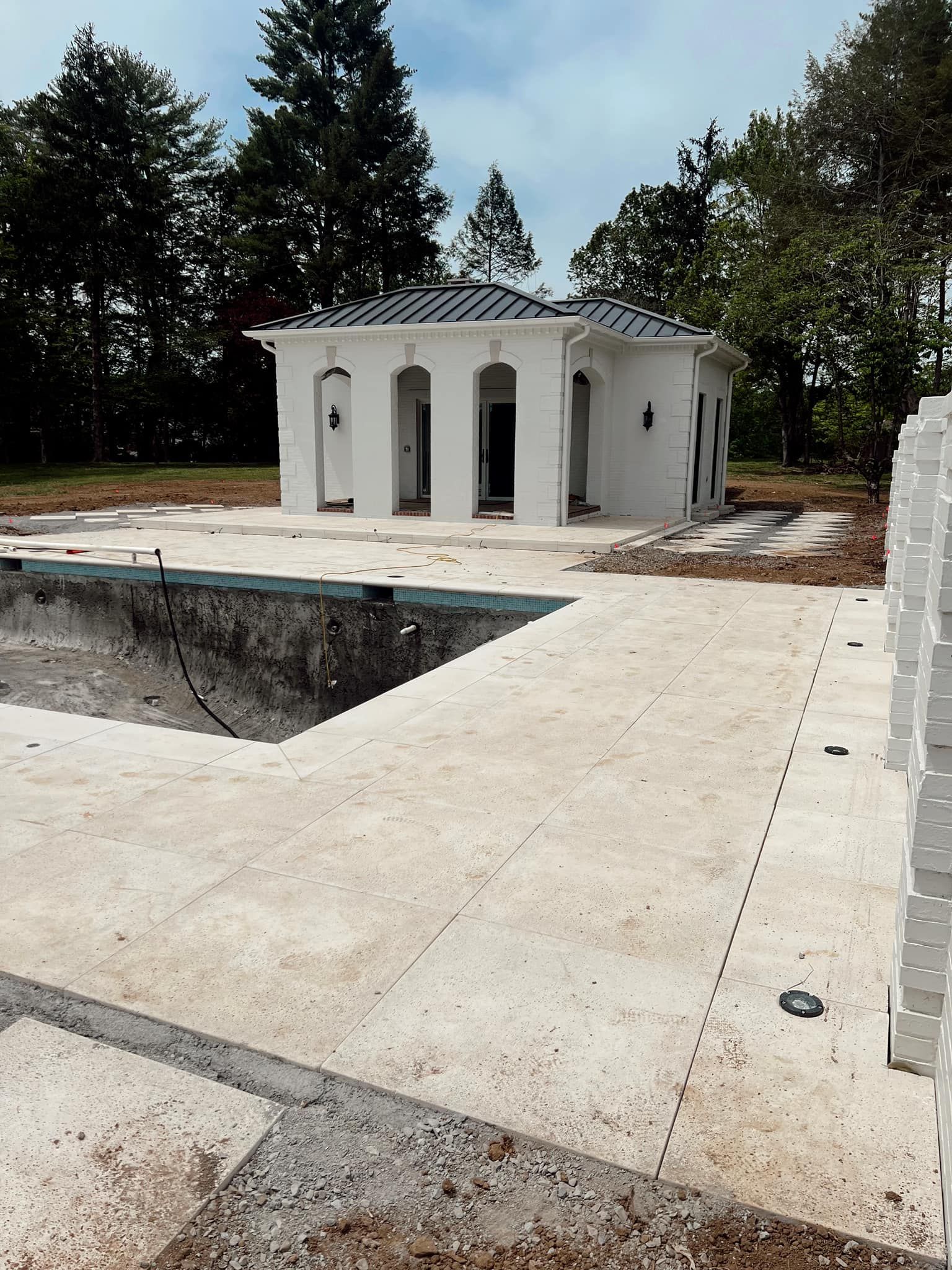 White octagonal pool house beside an unfinished concrete pool deck with trees in the background