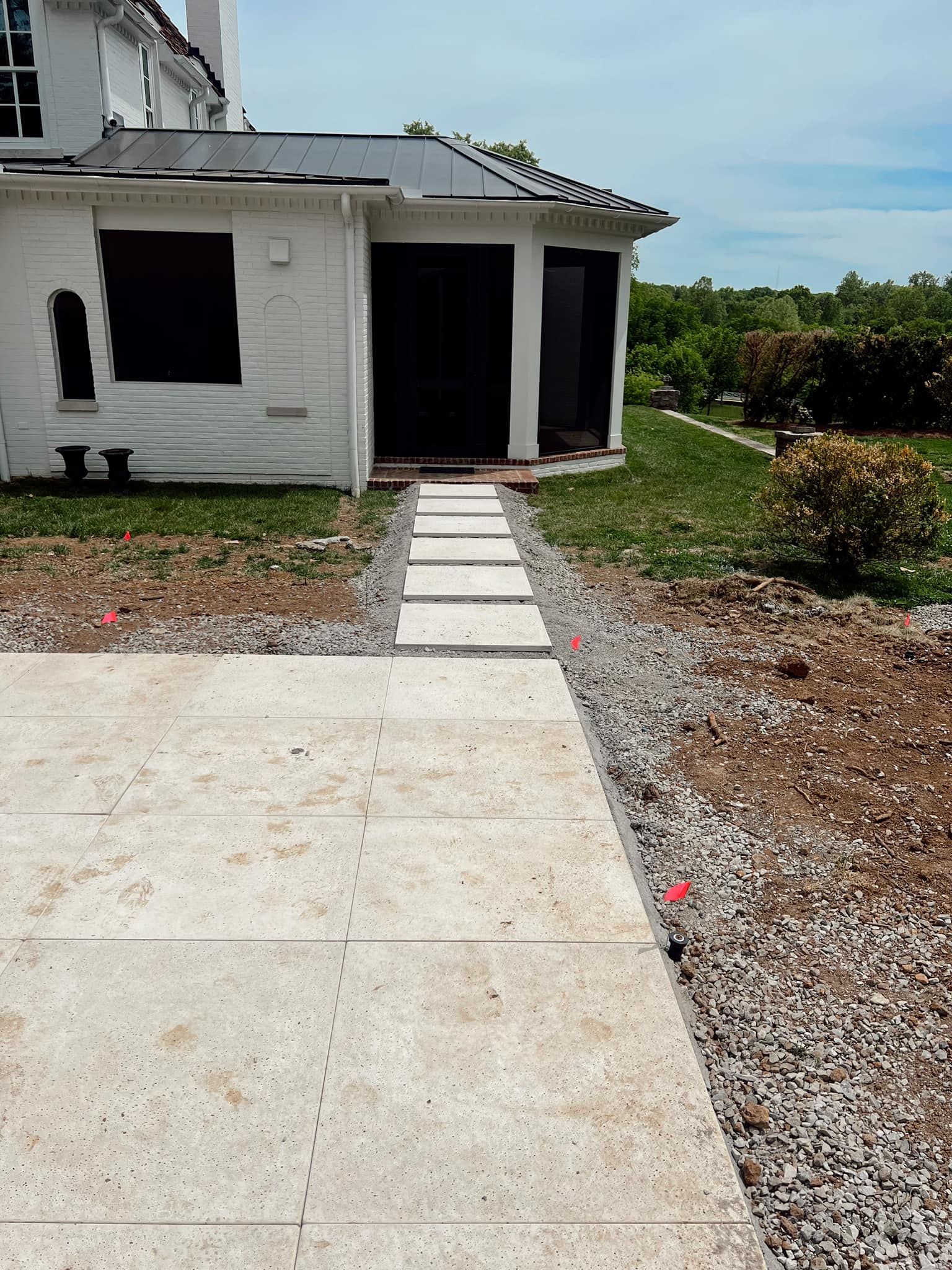 A small white house with a concrete walkway leading to the front door, surrounded by gravel and grass.