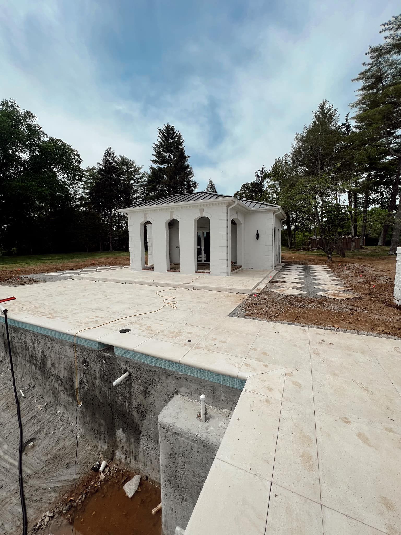 White unfinished building on a concrete slab in an outdoor wooded area under a cloudy sky