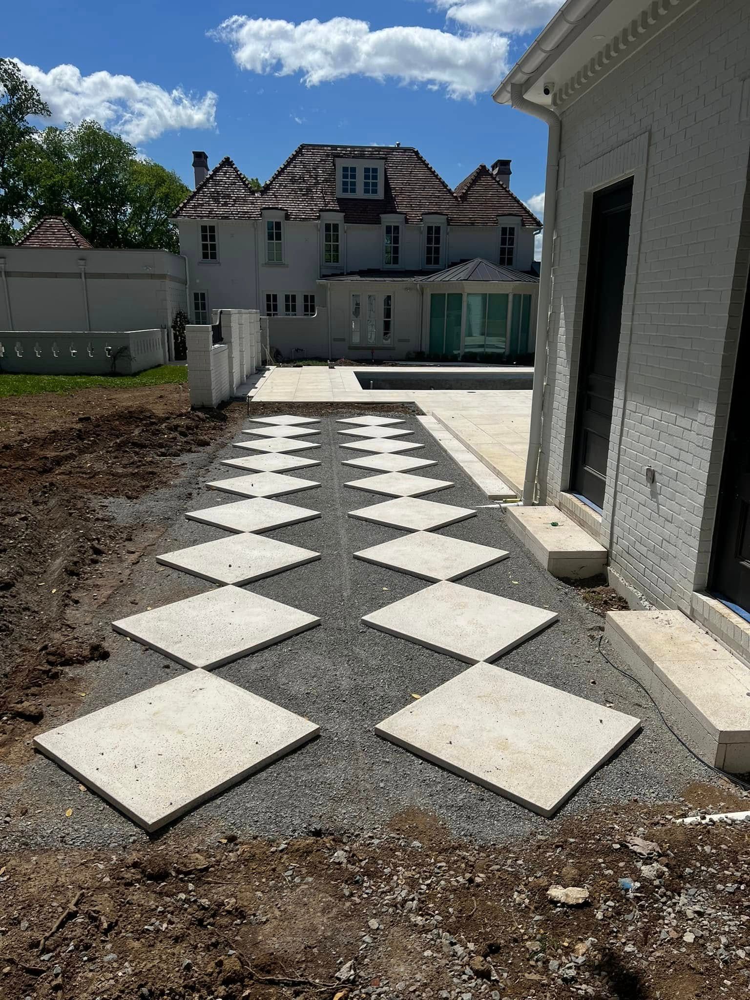 Checkerboard stone walkway leading to a house under construction, with gravel and unfinished landscaping.