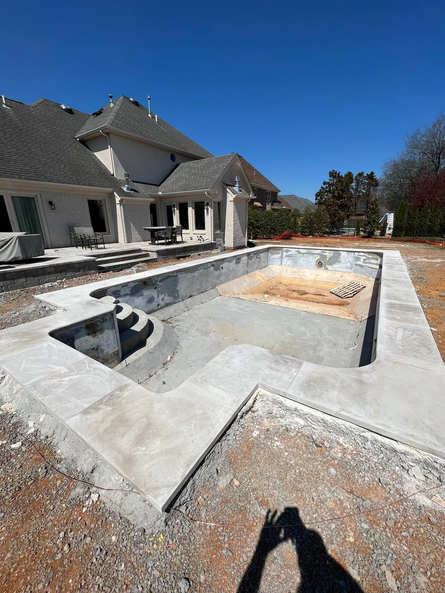 Empty concrete backyard pool under construction beside a house on a sunny day