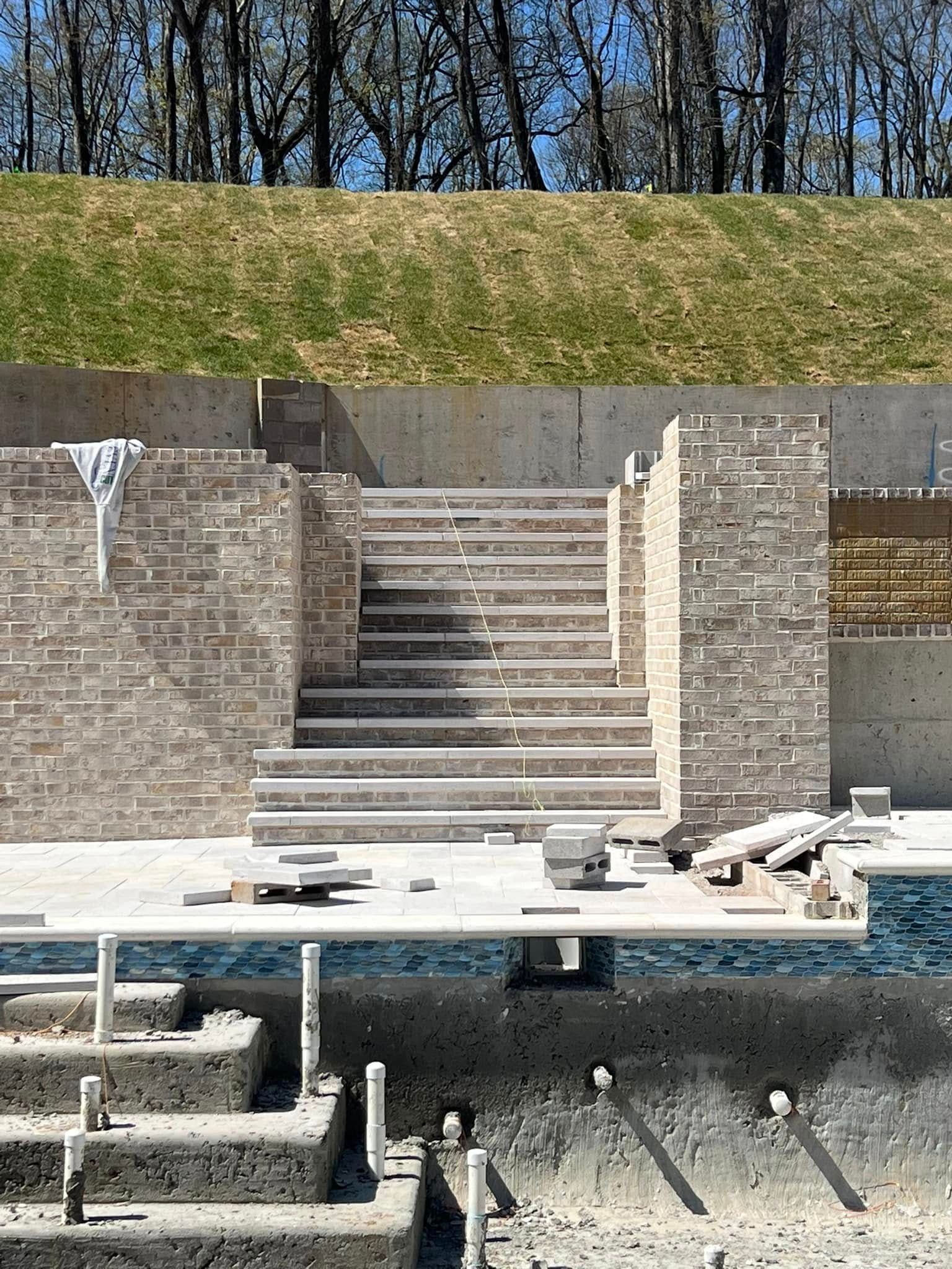 Brick stairway between retaining walls with grassy embankment above and construction materials in foreground