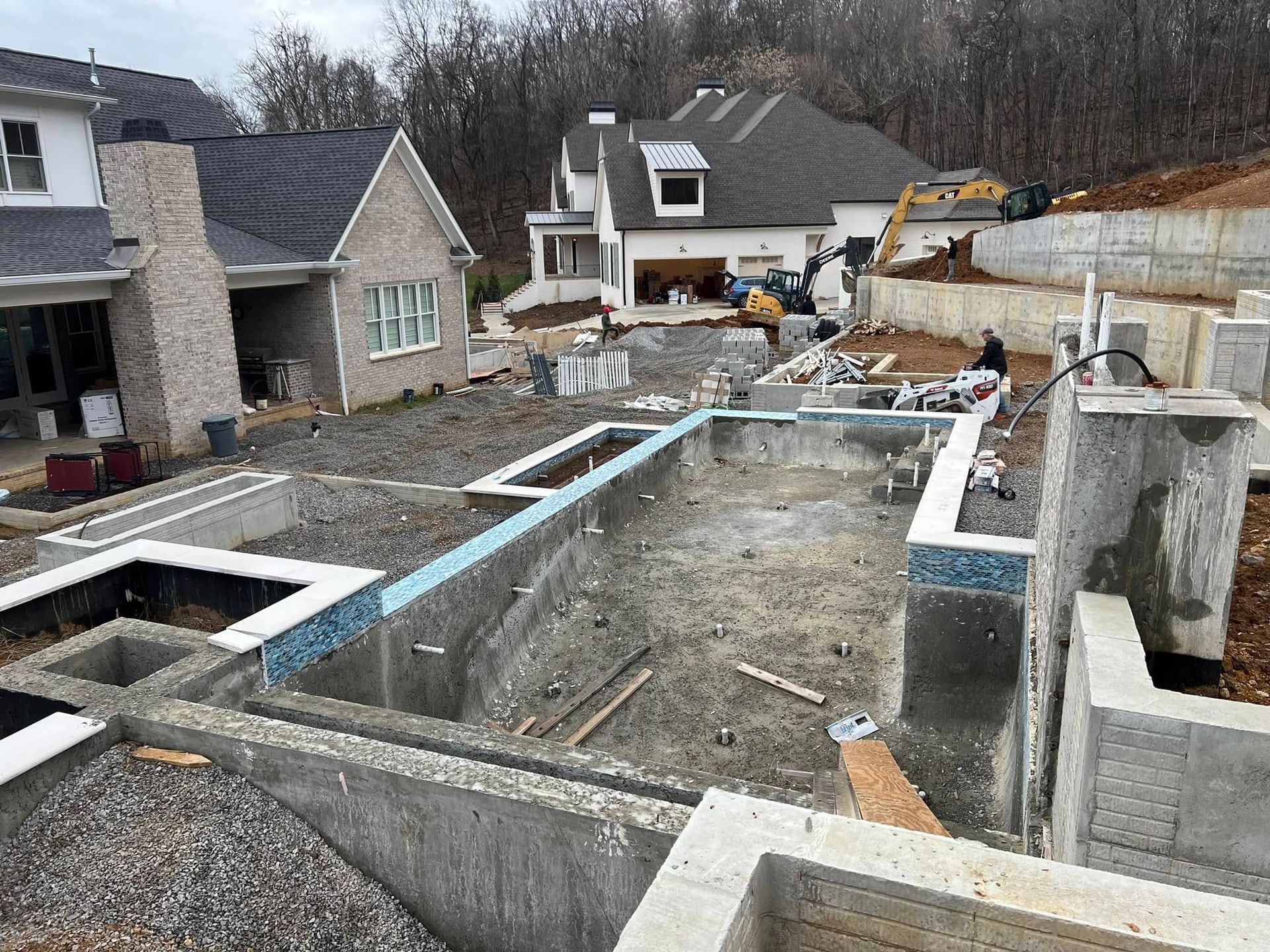 Concrete foundation site with excavated trenches, retaining walls, and houses in the background